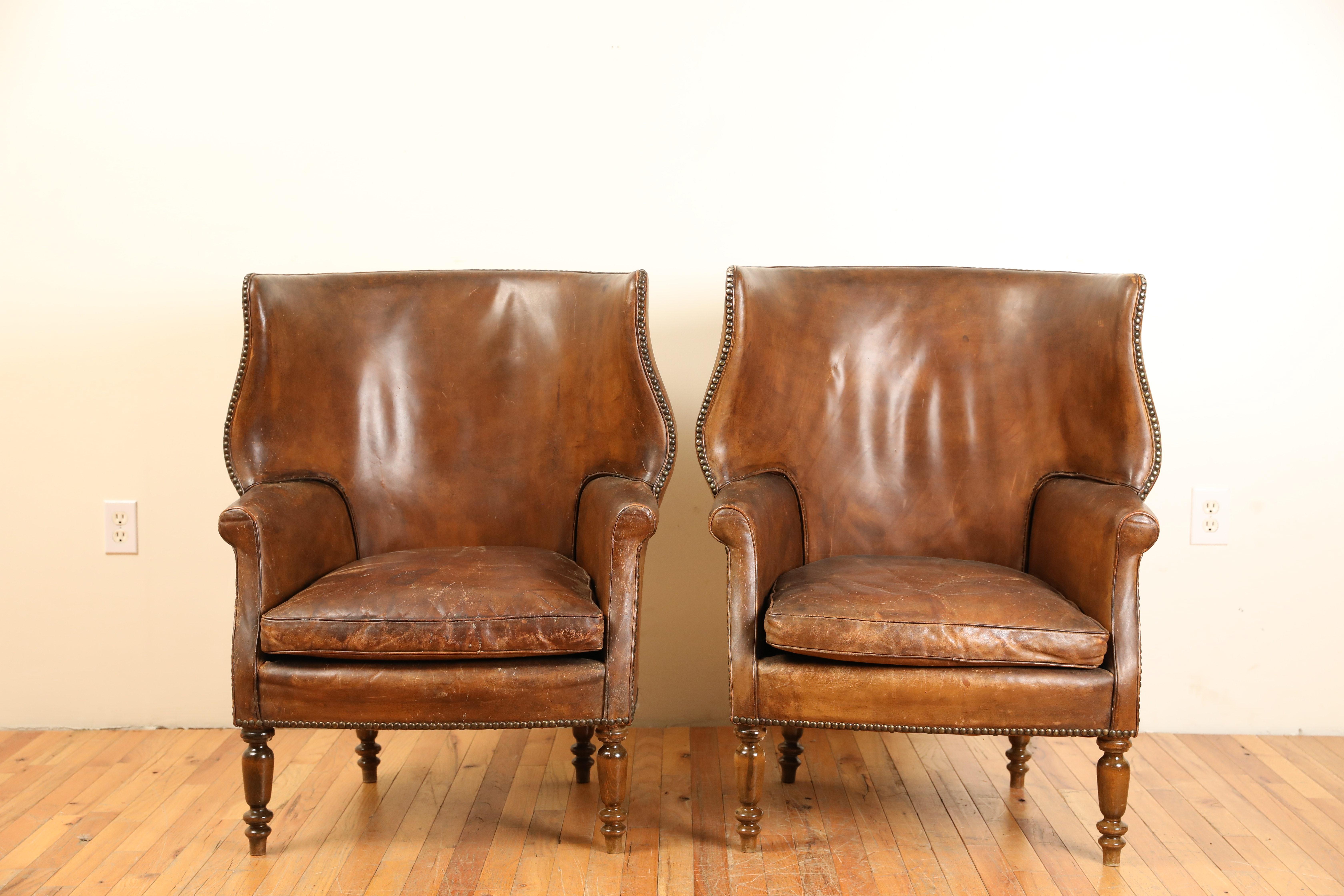Upholstered completely in leather these wing chairs have loose cushions, are in very good condition, and are raised on turned tapering legs