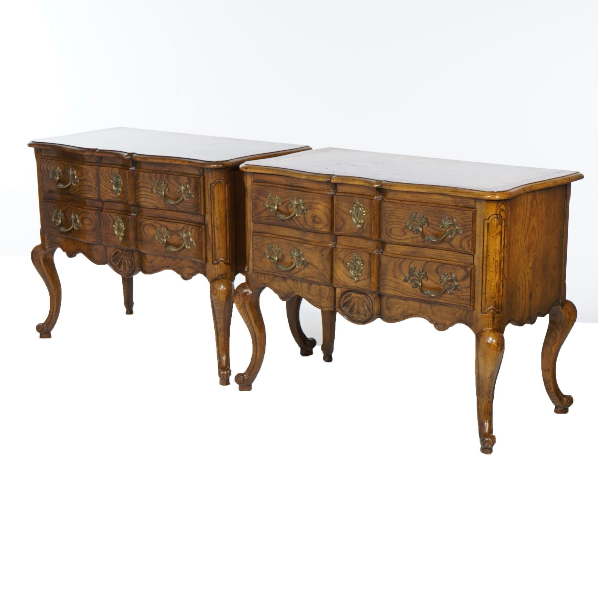 A pair of lowboy French Lois XV style chests by Baker offer oak, burl and walnut construction in serpentine form with two drawers, each with foliate cast hardware, raised on cabriole legs terminating in scroll form feet, maker label as photographed,