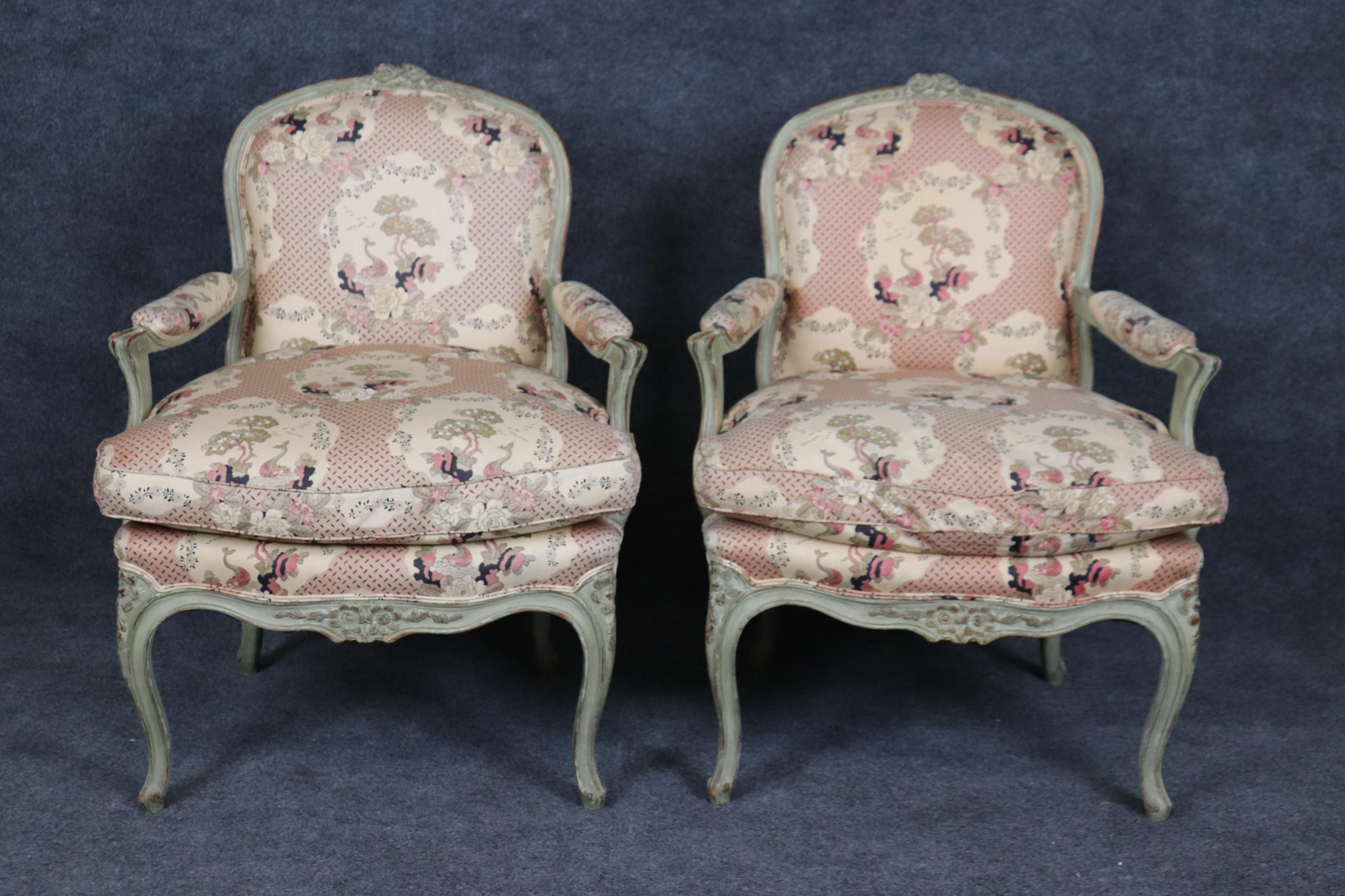 This is a beautifully carved pair of French made bergere chairs in gray paint. The chairs feature chinoiserie style upholstery. Measures 36.5 tall x 27 wide x 26 deep x seat height 21 inch tall. The chairs date to the 1920s era and will show wear to