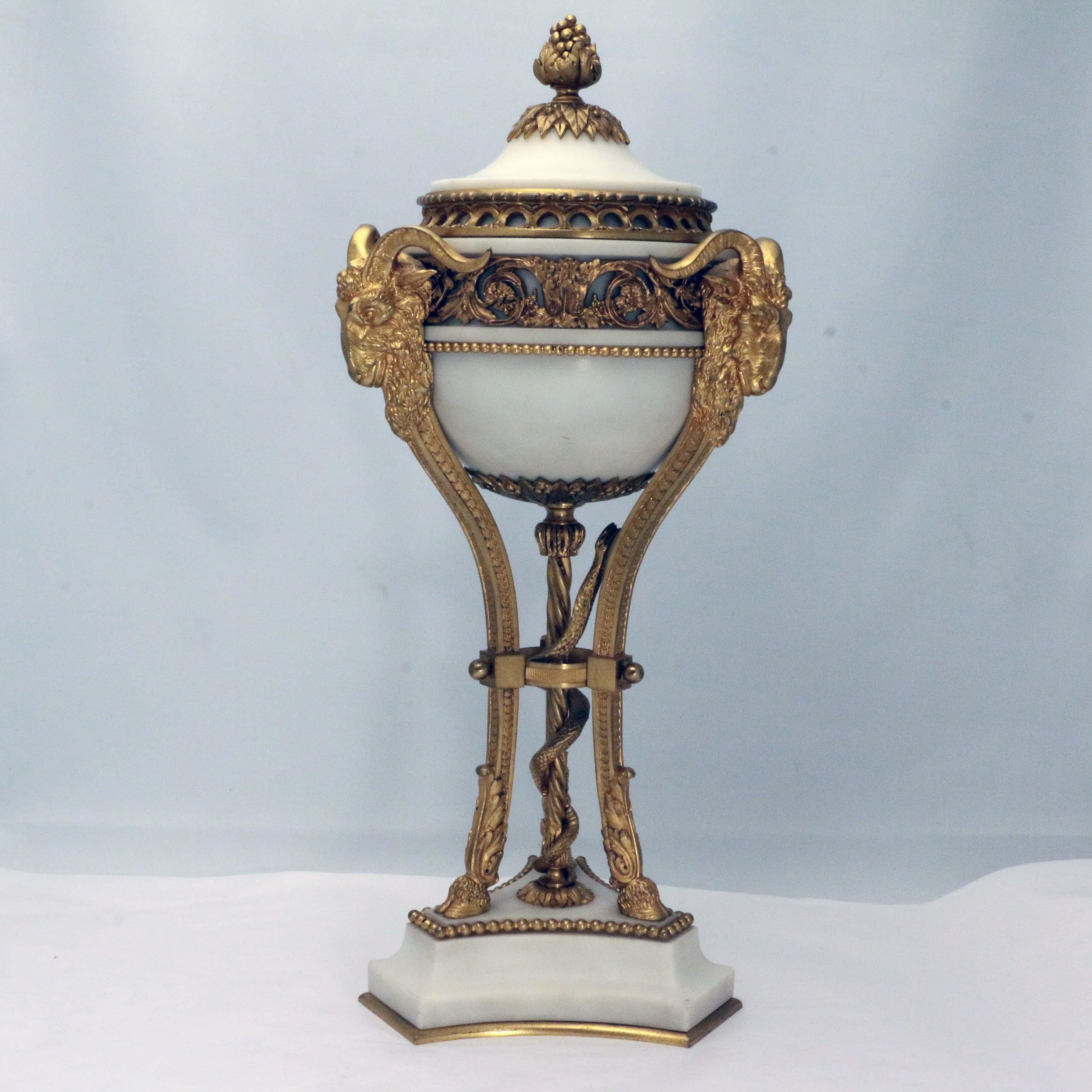 Pair of antique French Louis XVI marble and gilt bronze covered urns, each  embellished with foliate garlands and berried finial, applied with rams' masks raised on animal leg supports surrounding spiral column and serpent,  the tripartite incurving