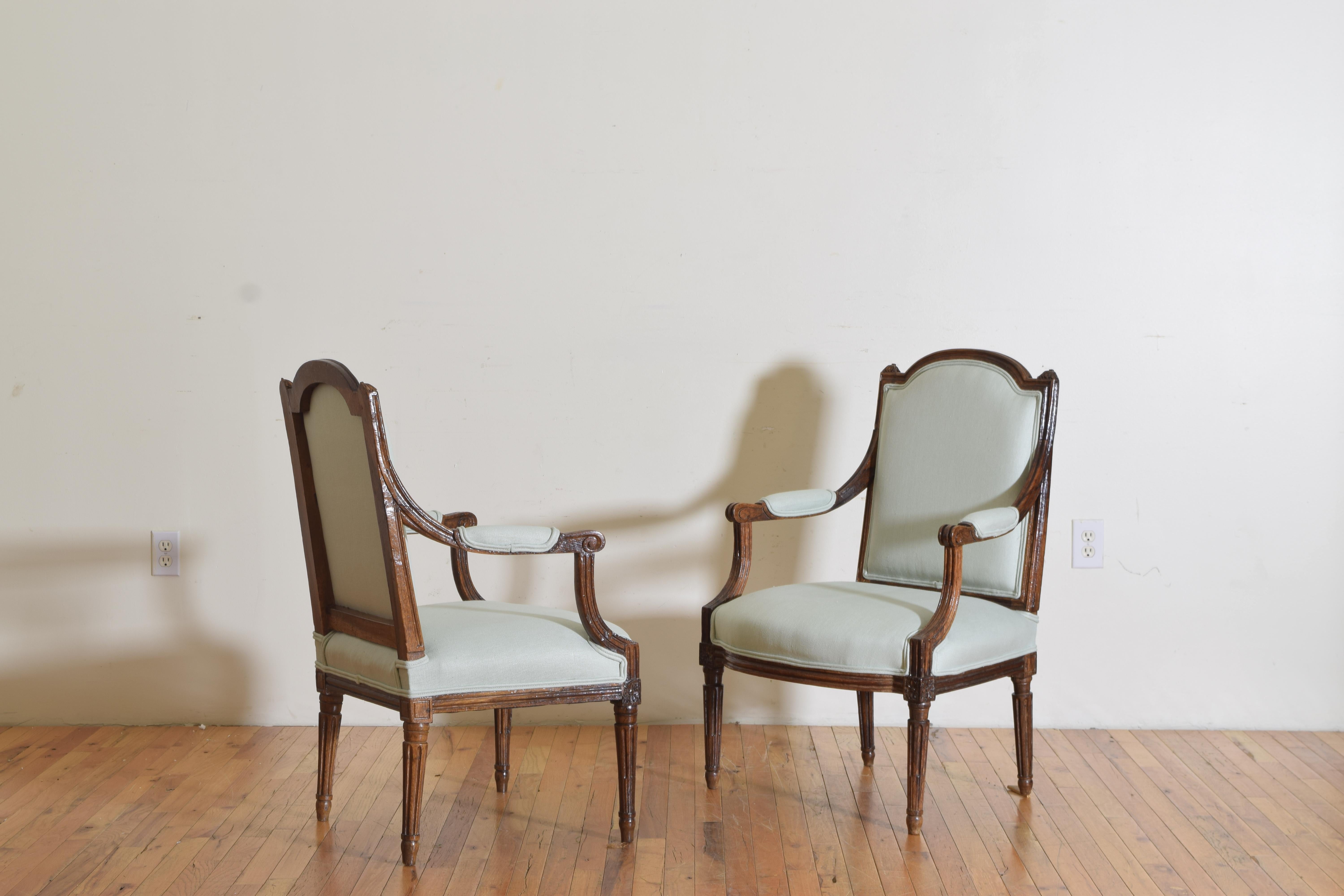 The chairs having arched backrests between small carved finials, upholstered backs and seats, the arm supports fluted as are the round tapering legs.