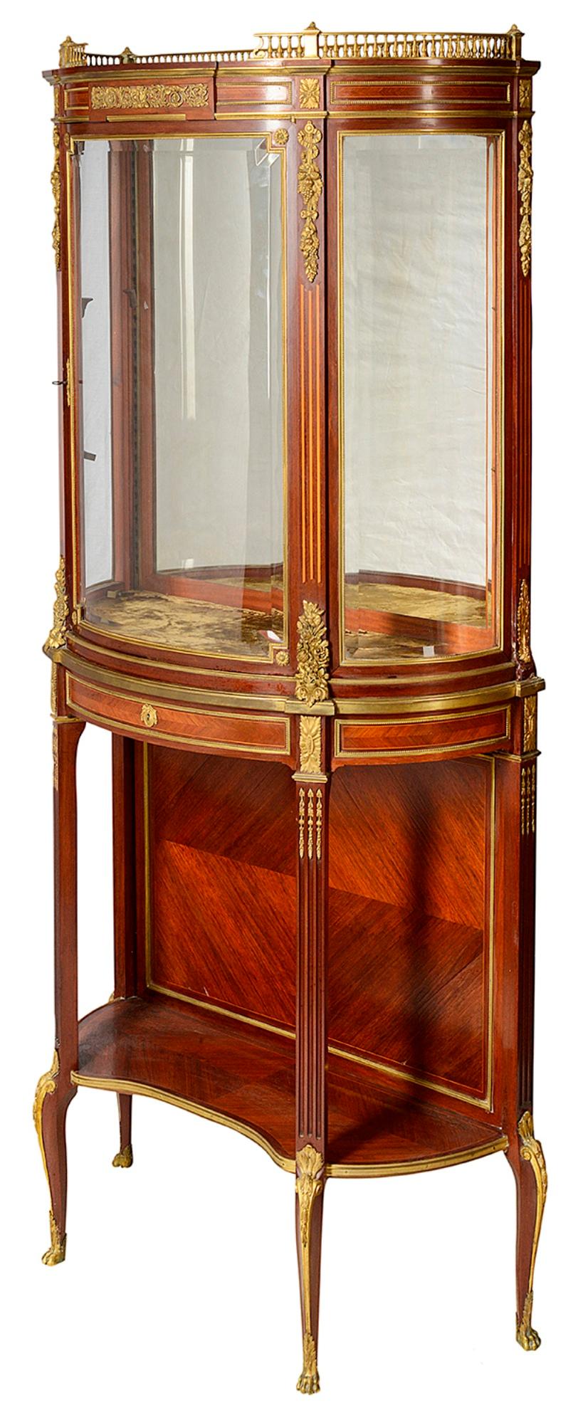 A very good quality pair of late 19th century French mahogany bow fronted display cabinets, each with a gallery to the top, gilded ormolu foliate and molded mounts, central doors with a glass shelf within, a frieze drawer above a shelf beneath with