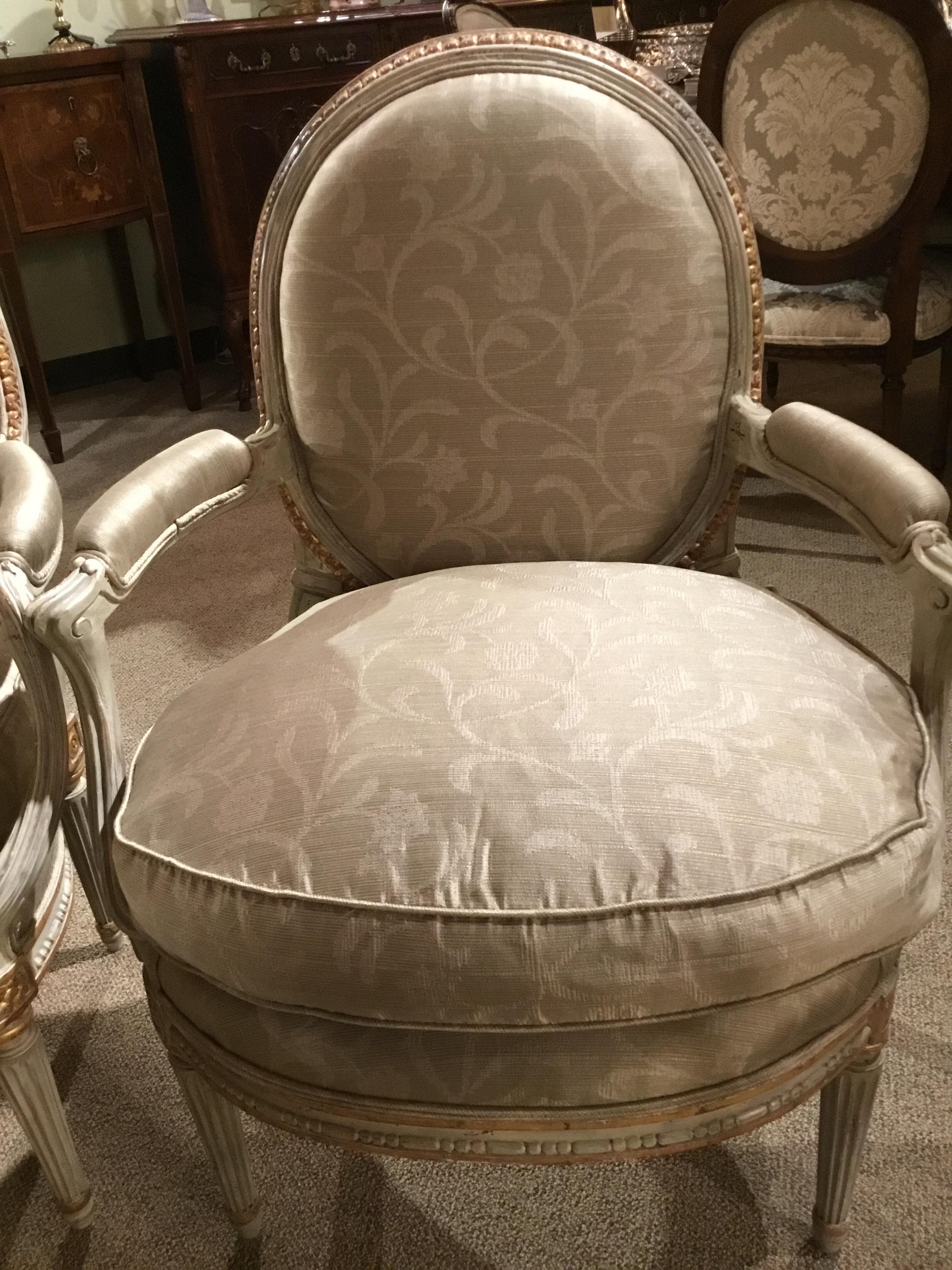 Early 19th century pair of Louis XVI style chairs with new upholstery in beige foliate 
Design fabric. Parcel paint in cream color with original gilt enhancement.
Tapered and reeded leg. Oval back.