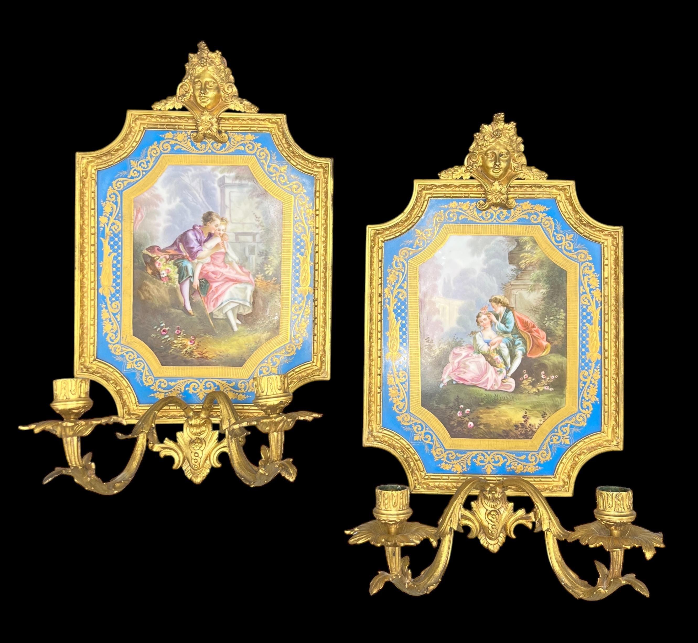 Pareja de apliques franceses antiguos (finales del siglo XIX) de dos luces de estilo Luis XV, de bronce dorado con placas de porcelana finamente doradas y pintadas con escenas pastorales de amantes cortejándose.  Cada una de 16 por 9 1/4 por 6