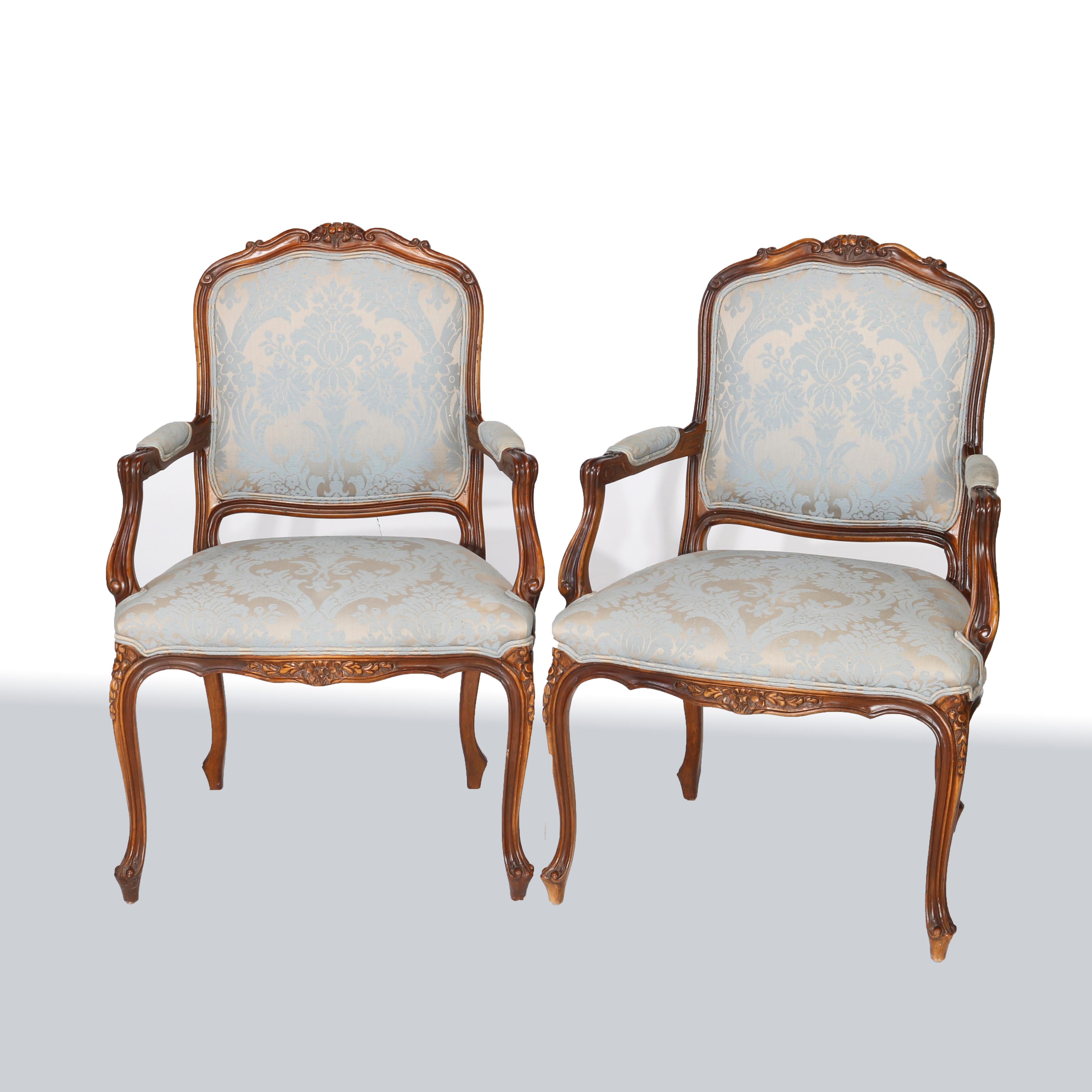 A matching pair of French Louis XV style upholstered fauteuil arm chairs offer fruitwood construction with foliate carved crest over scroll form frame having shaped back, covered arms and raised on cabriole legs terminating in scroll form feet, 20th