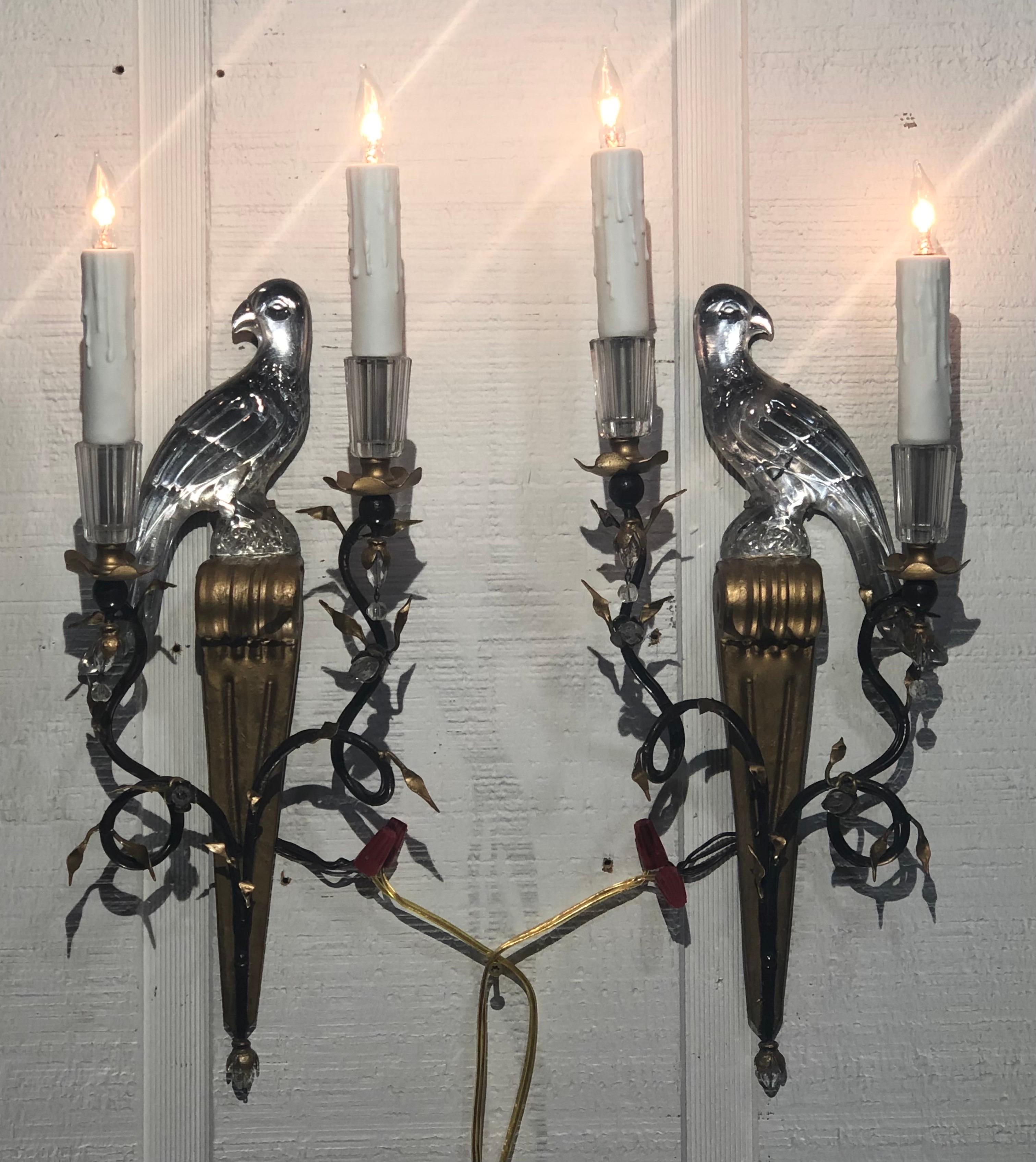 This Regal pair of Maison Baguès Tôle and Crystal Parrot Wall Sconces with  Foliage Branches were made in France in the early Twentieth Century.  Each of the opposing Baguès Wall Sconces have a hand-carved Crystal Parrot with Silvered Backs that are