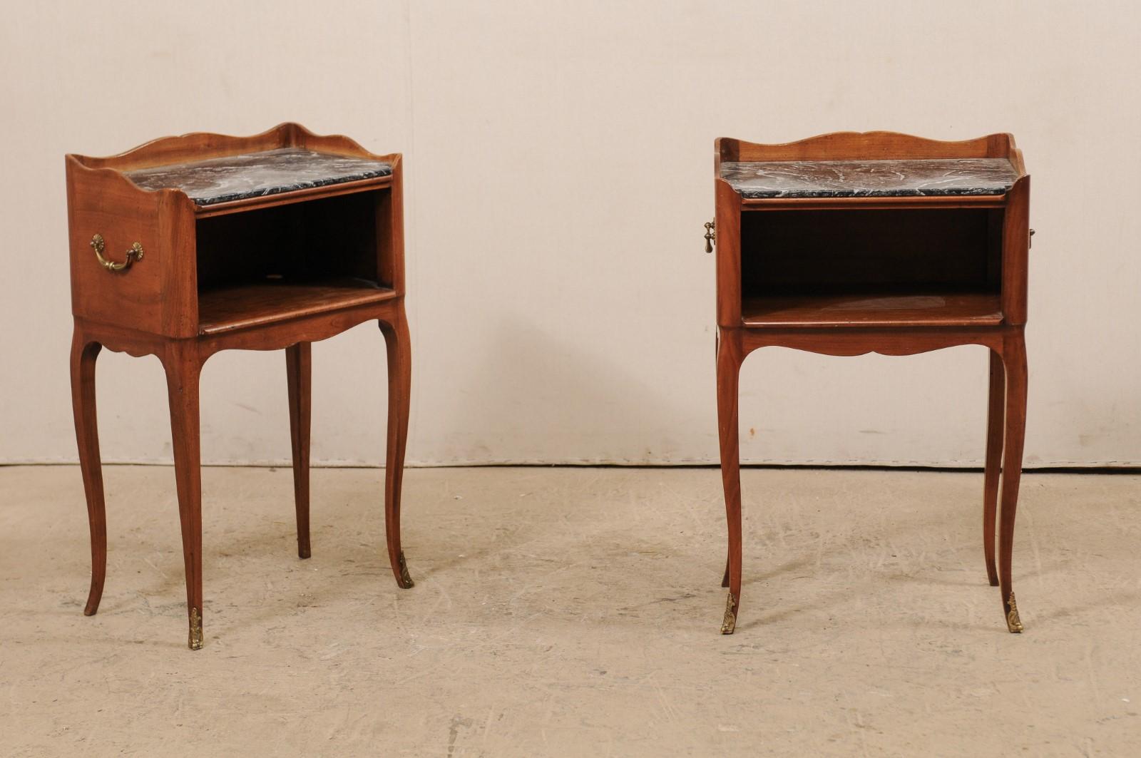 A pair of French side chests with marble tops from the mid-20th century. This pair of vintage stained wood bedside tables from France each feature a shapely raised (along the sides and rear) top rim with marble seated inside, resting above an open