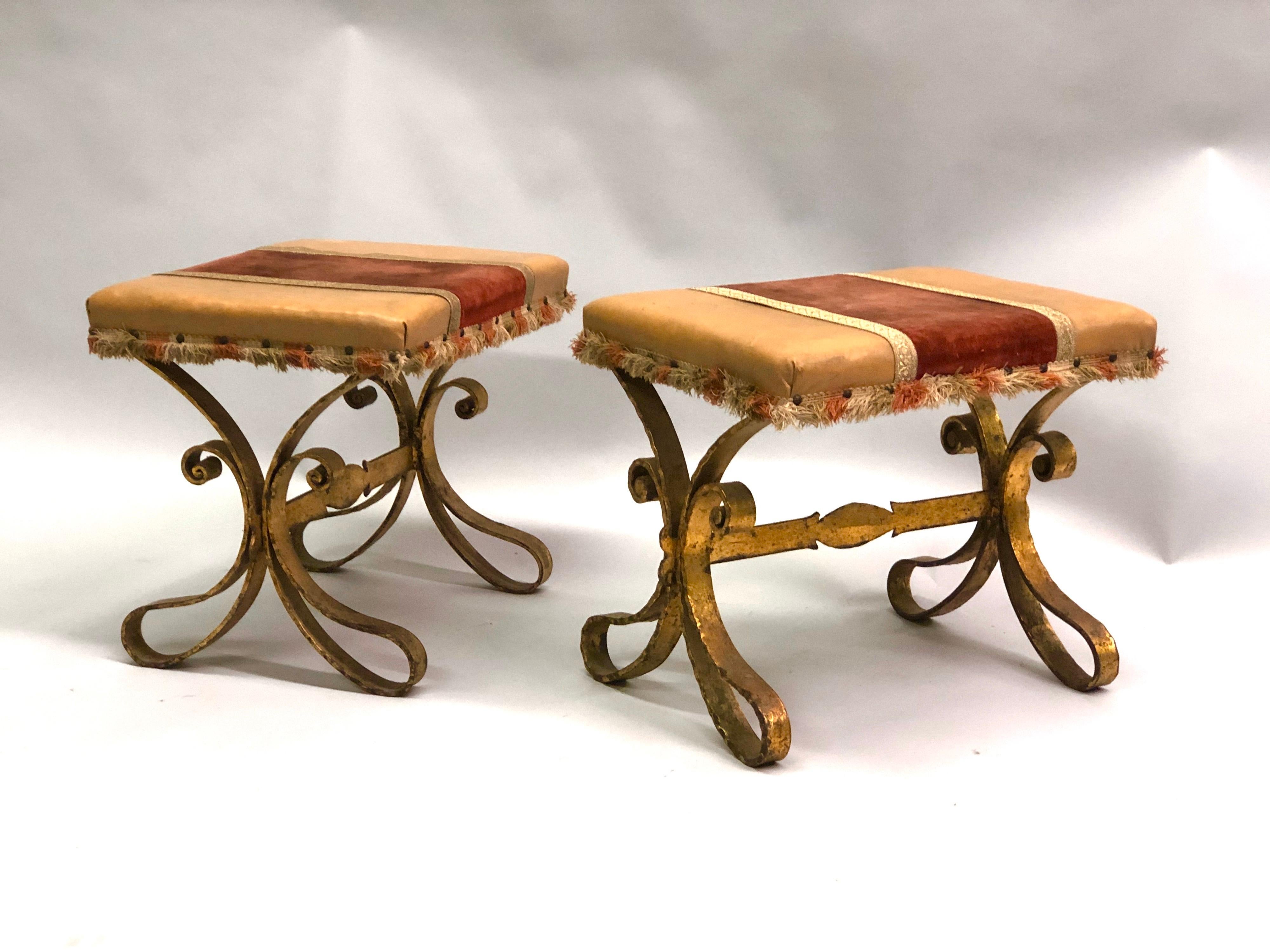 Pair of French Mid-Century Modern gilt wrought iron and leather benches or stools or ottomans in the style of Gilbert Poillerat. 

The pieces are handmade in hand-hammered iron and hand gilt. Seats are partially covered in leather.

References: