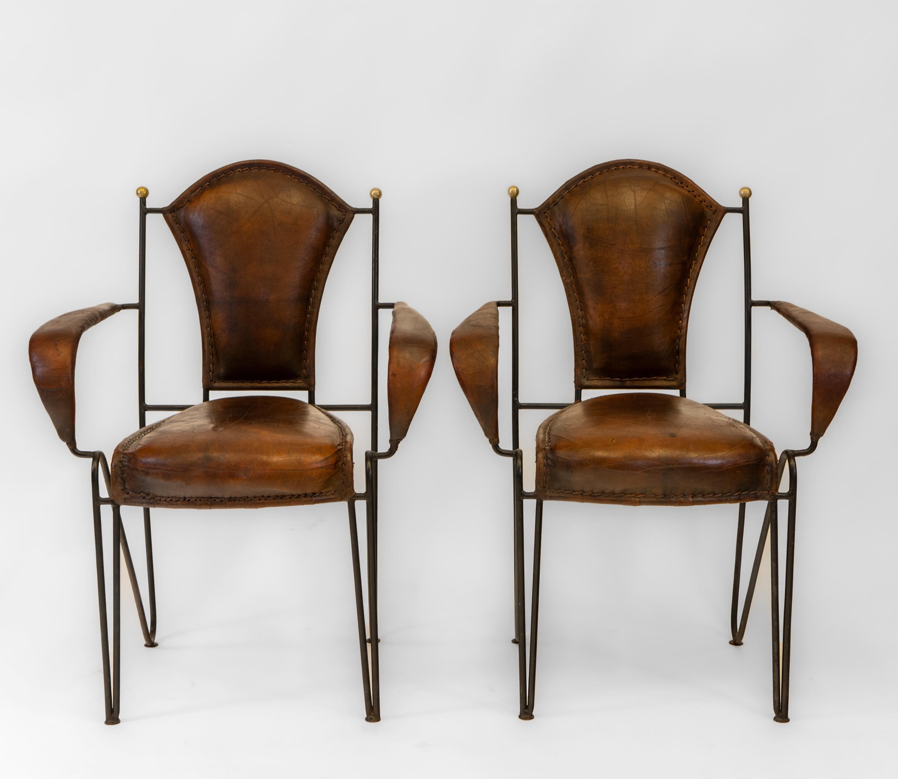 Fabulous pair of mid century French leather & iron armchairs. Circa 1950’s.

Another pair are available listed separately, also as a set of four.

The chairs have brass ball finials leading to iron sculptural frames, with hair pin legs. They boast