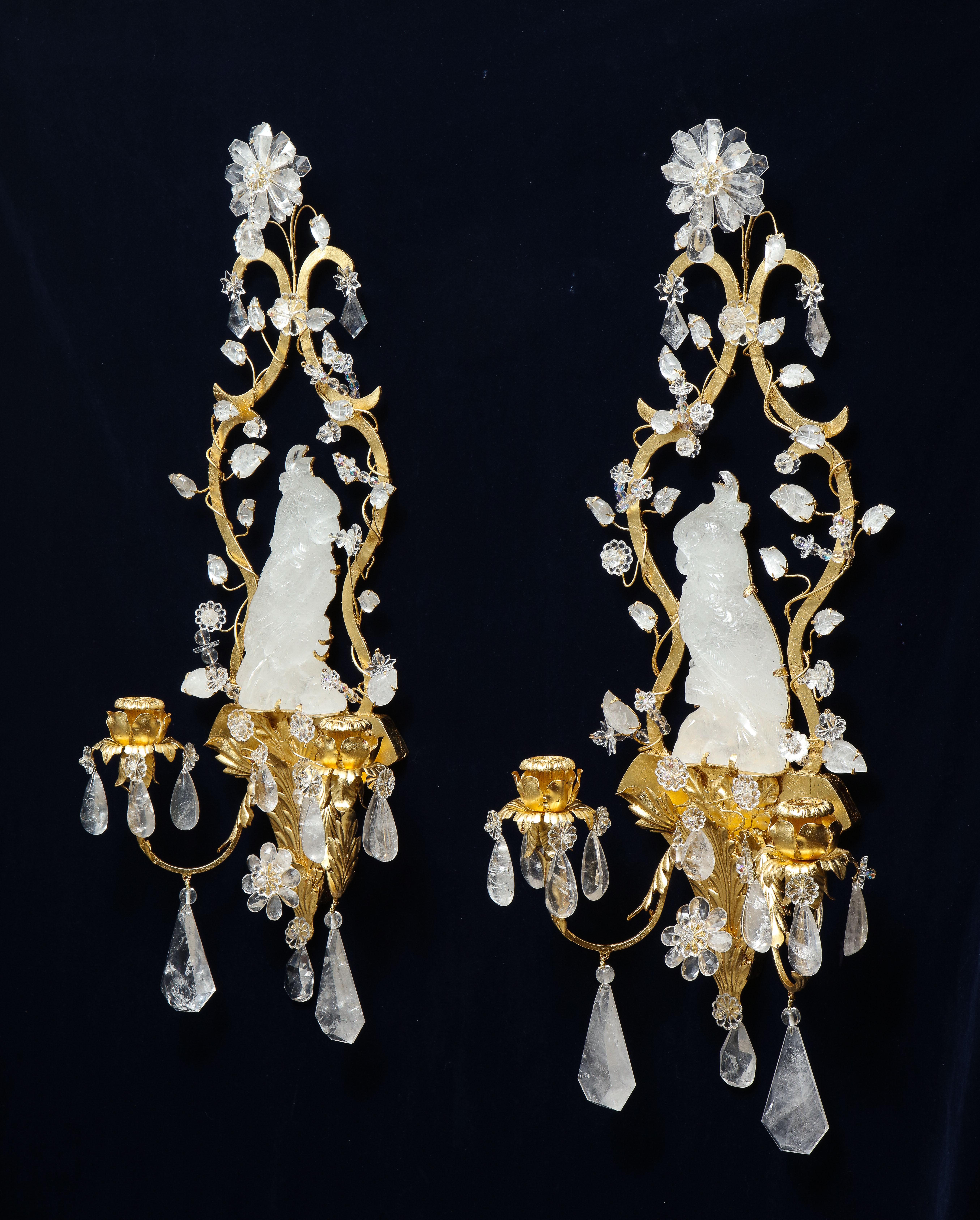 A fabulous pair of French Mid-Century Modern Louis XVI style and Bagues style cockatoo-form rock crystal and 24k gilt metal wall appliques/sconces. Each of these sconces is modeled after the beautiful cockatoo bird. The center of the sconces is