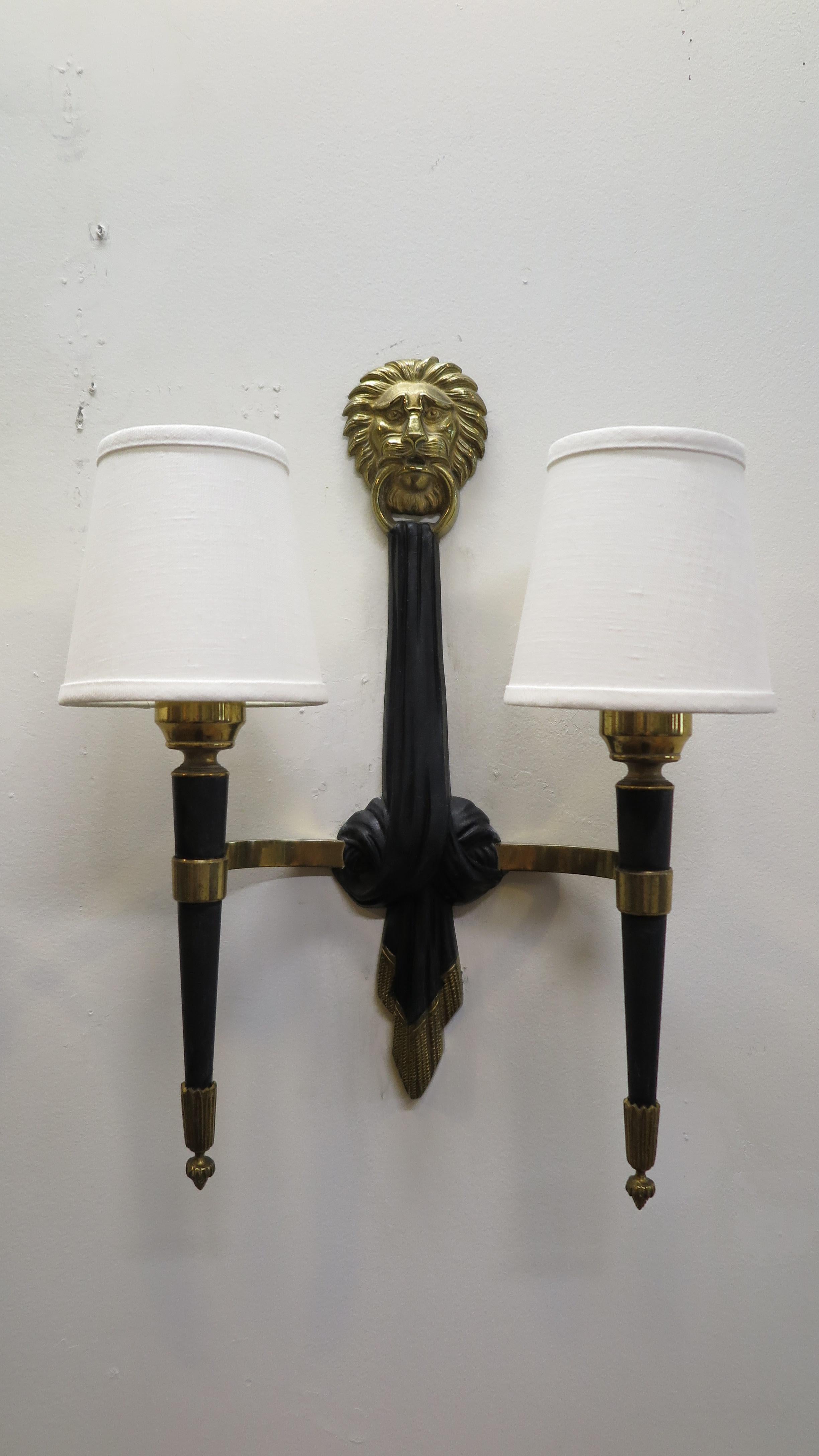 Pair of French midcentury sconces attributed to Maison Jansen. Elegant brass and bronze lion topped sconces with two lights each with Linen shades. Very good condition rewired for US.