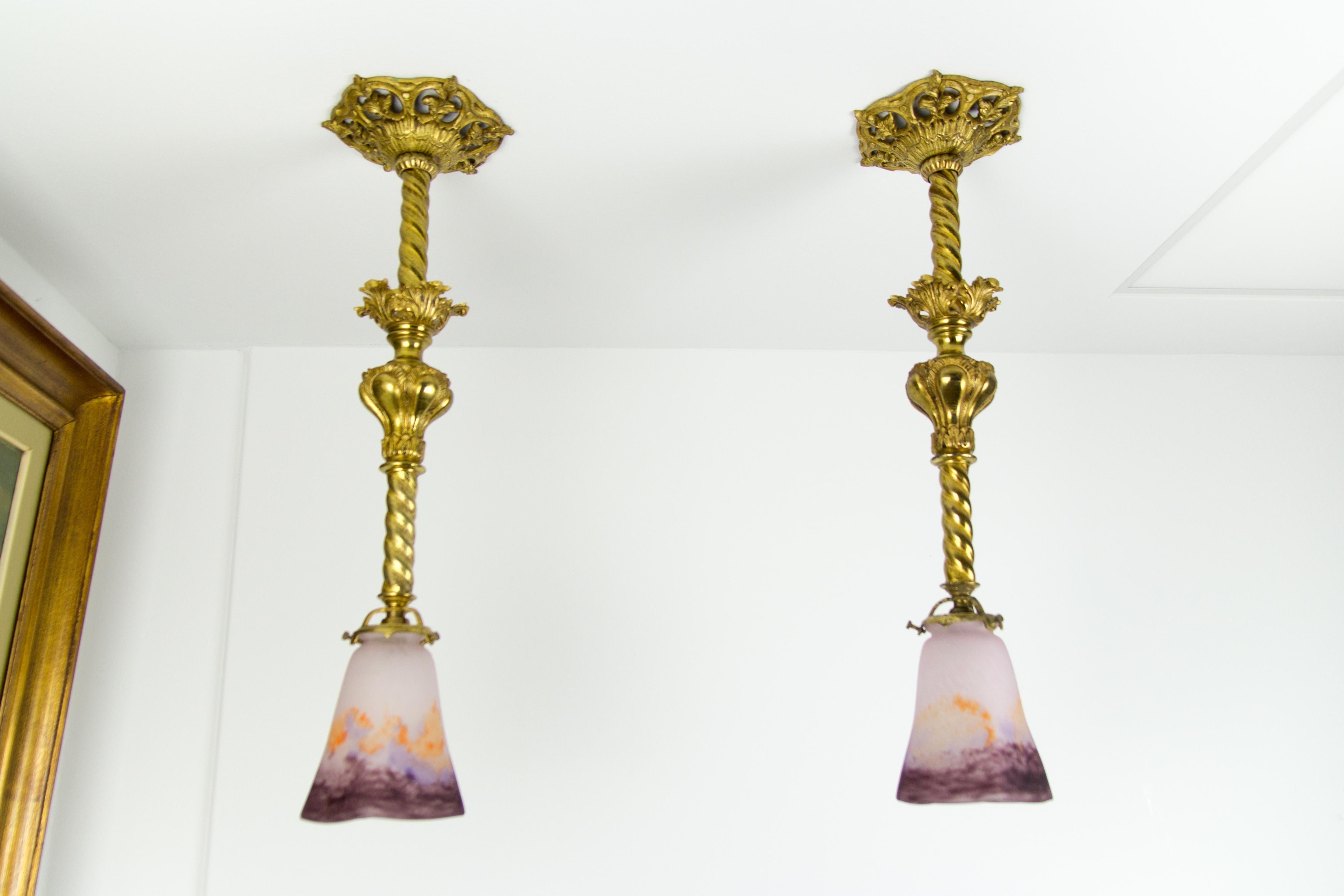 An impressive pair of early 20th-century ornate gilt bronze pendant light fixtures with Pate de Verre glass shades in purple and orange, signed in the glass “Muller Strasbourg”. Each pendant light fixture has one socket for a B22-size light