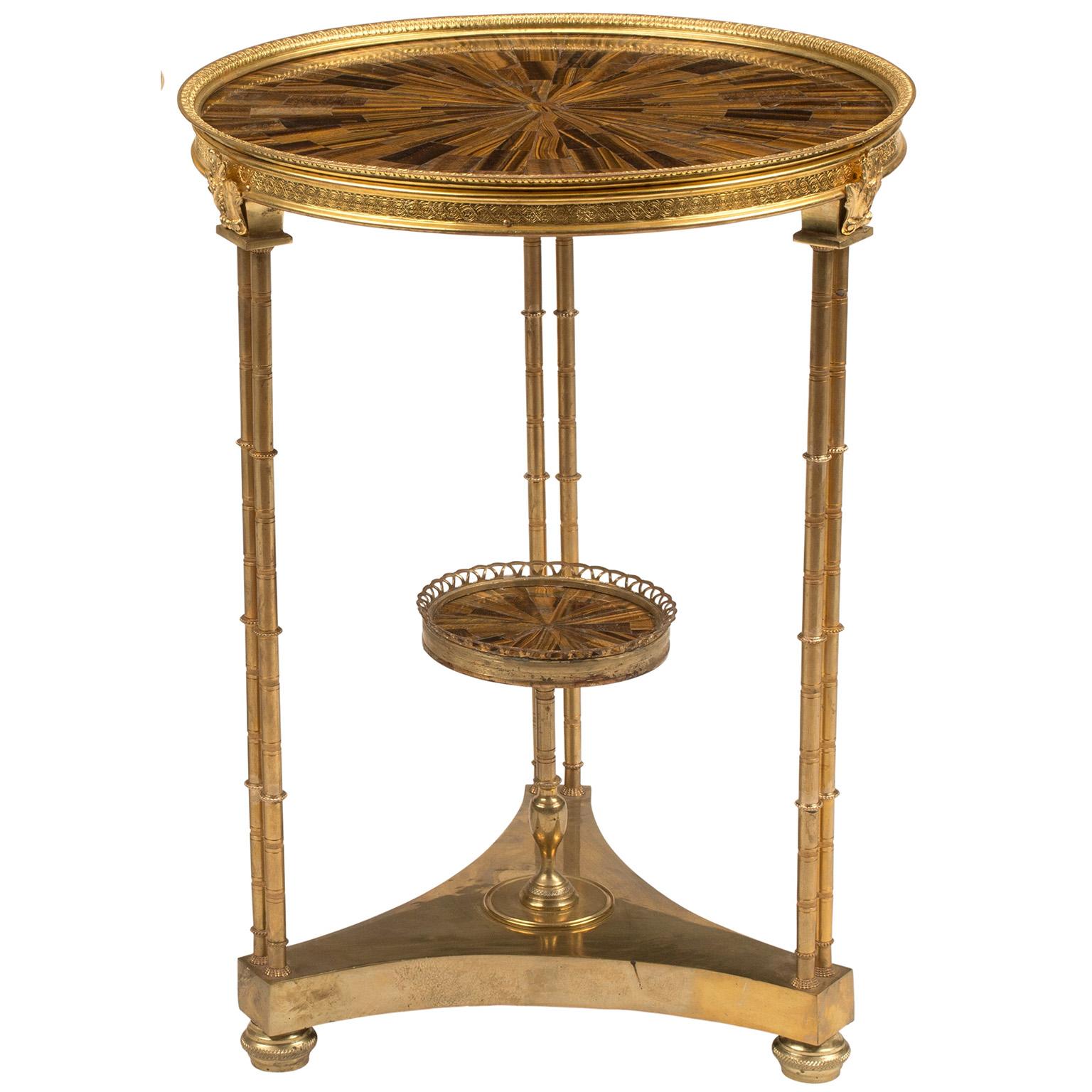 Pair of neoclassical revival style gilt bronze and gilt metal two-tier guéridons round end or side tables with tiger-eye inlaid tops. The triform gilt-bronze bases, topped with a circular cast-chased gilt-bronze rim and fitted with a symmetrically