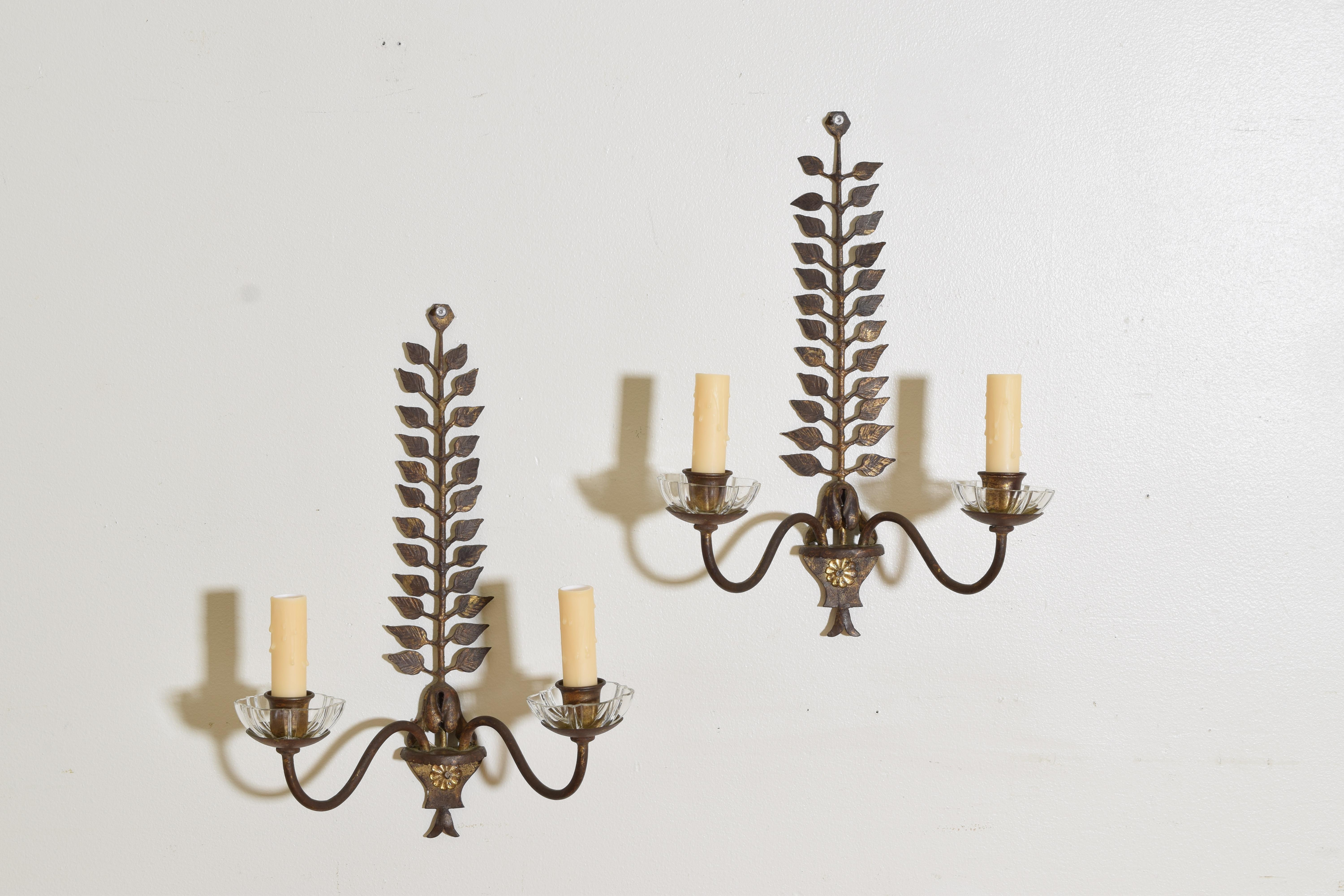 A pair of previously gilded 2-light wall sconces with leaves of cut metal in tapering columns with glass bobeches and glass rosettes at the bases