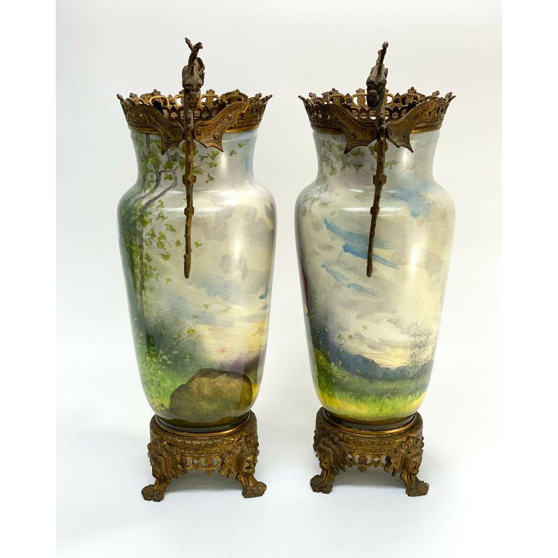 Pair French Porcelain Twin Handled Gilt Bronze Mounted Urns, Hand Painted, c1900

The central area of the urns depict beautiful hand painted figures of a gentleman in burgundy red garbs and a maiden in a ruffled yellow ground- both in a forested