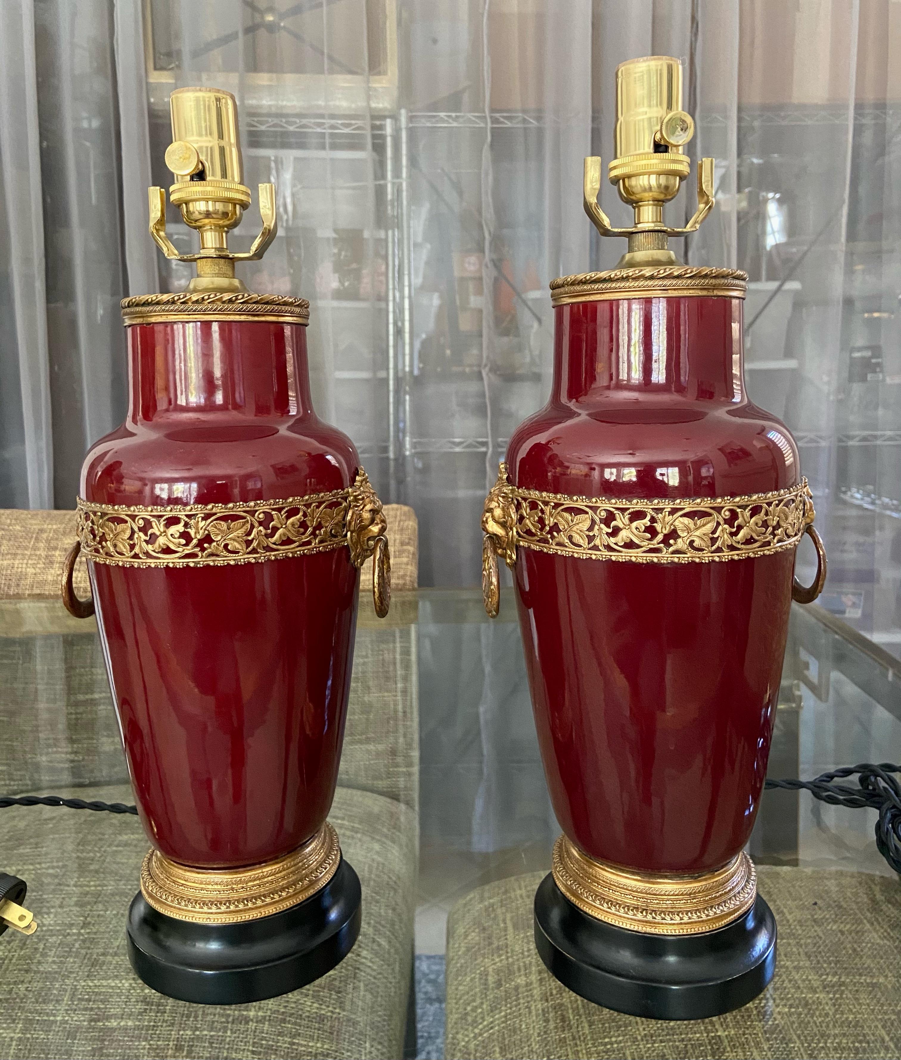 Pair of smaller scale early 20th century French Sang De Boeuf Oxblood vases converted as table lamps by Sarreguemines, France. Vases are adorned with finely detailed ormolu gilt bronze fittings including Lion heads with rings in their mouth. The
