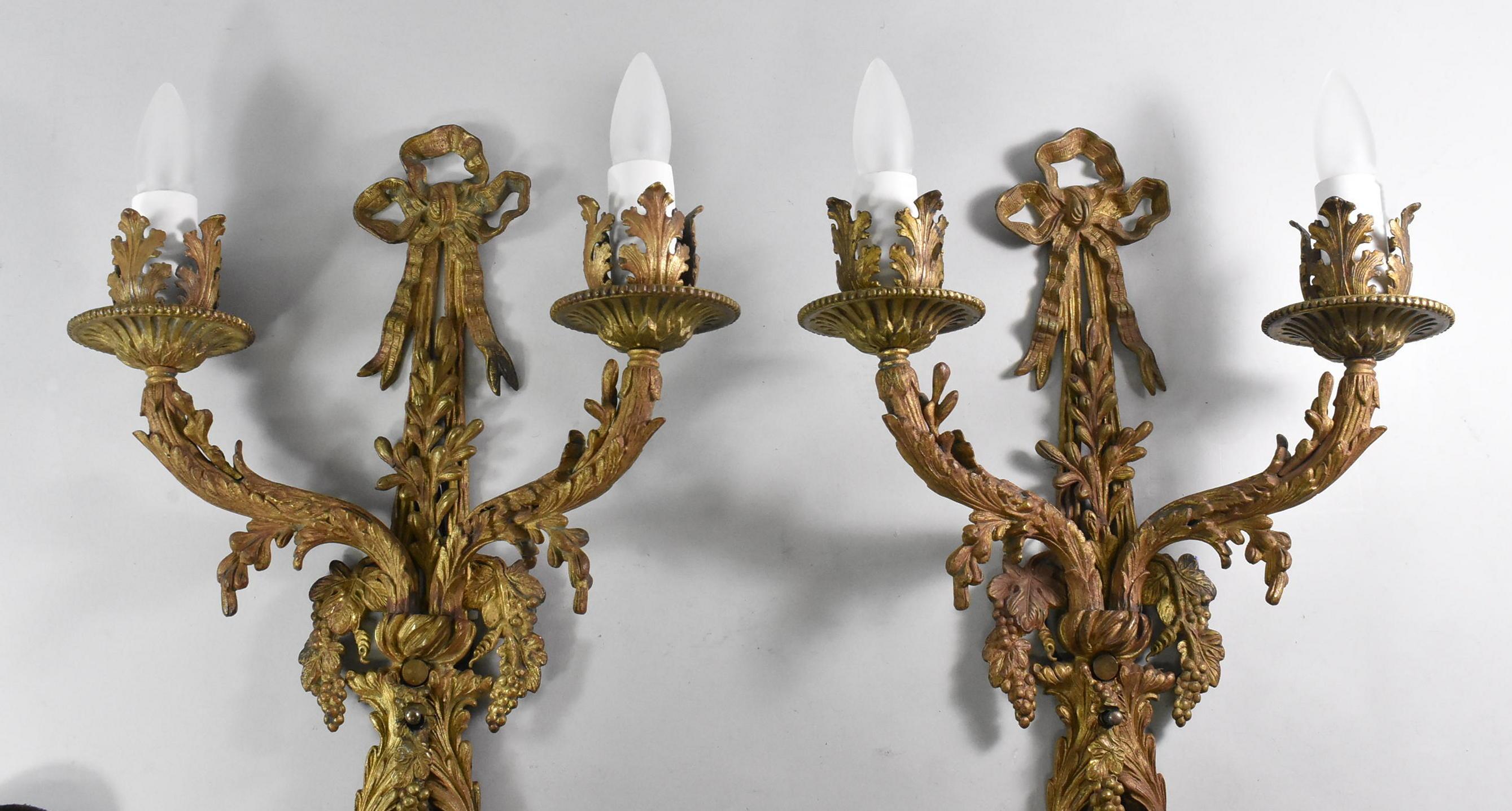 Pair of French style bronze two socket wall sconces. Ribbon bow top detail. Body has grape cluster with leaf designs. Acanthus leaf candleholder. Gold with variegated red patina. On off switch.