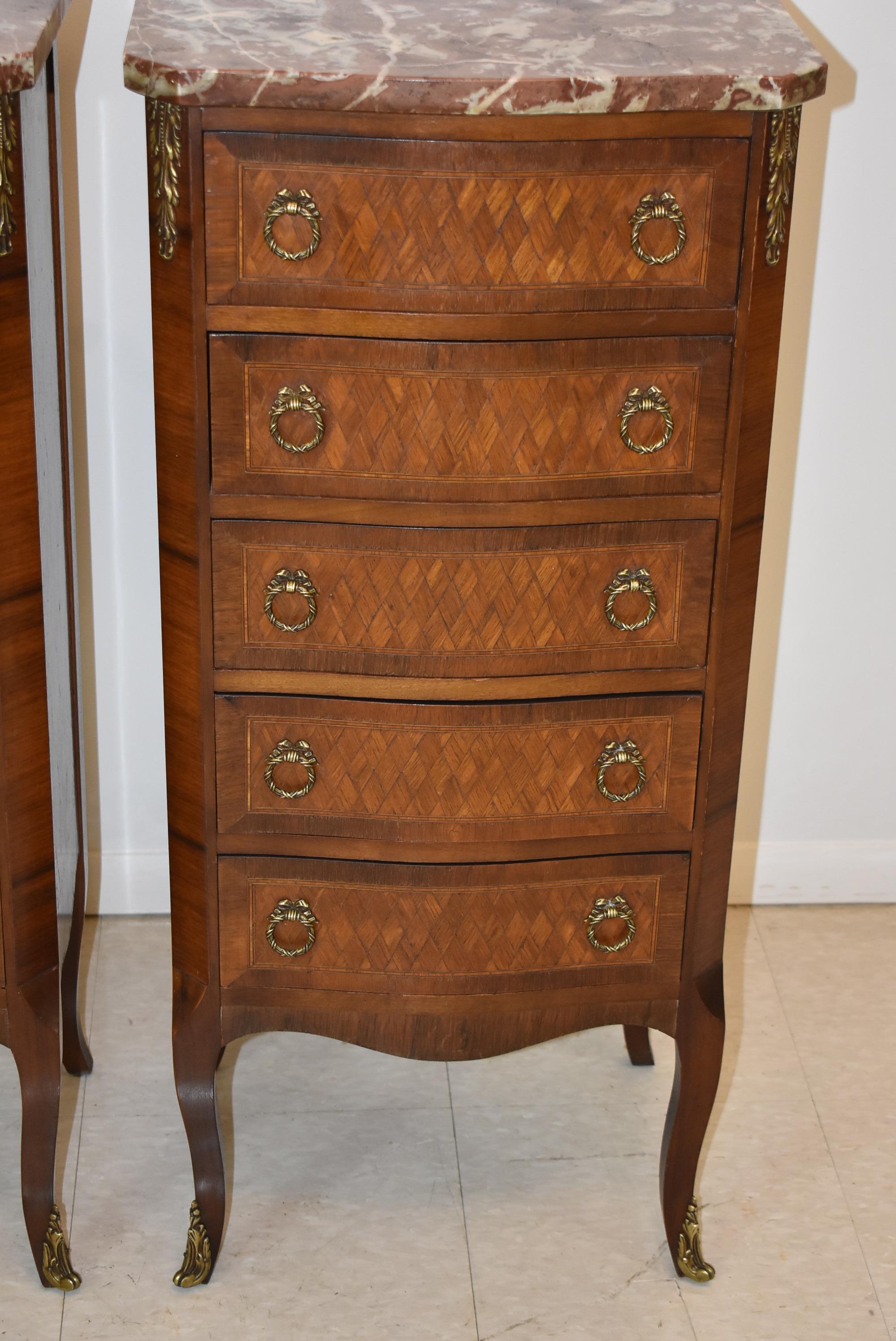 Pair of French style lingerie five drawer walnut chests with marble tops. Diamond pattern inlay woods on the drawer fronts and sides circa 1930s. Brass wreath shaped hardware with a bow. Italian marble tops. Dove tail drawer construction.