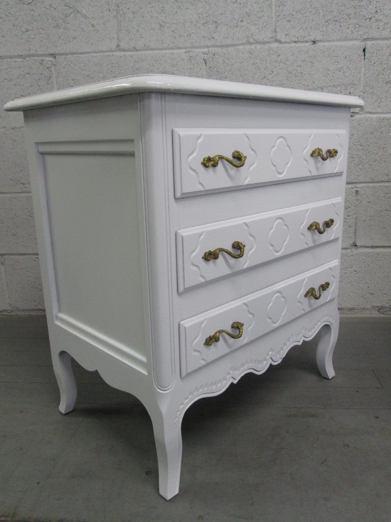 White painted pair of French style nightstands or chests. The nightstands have the original brass handles with a white lacquered finish. Would make a nice compliment to a French or Hollywood Regency inspired interior.