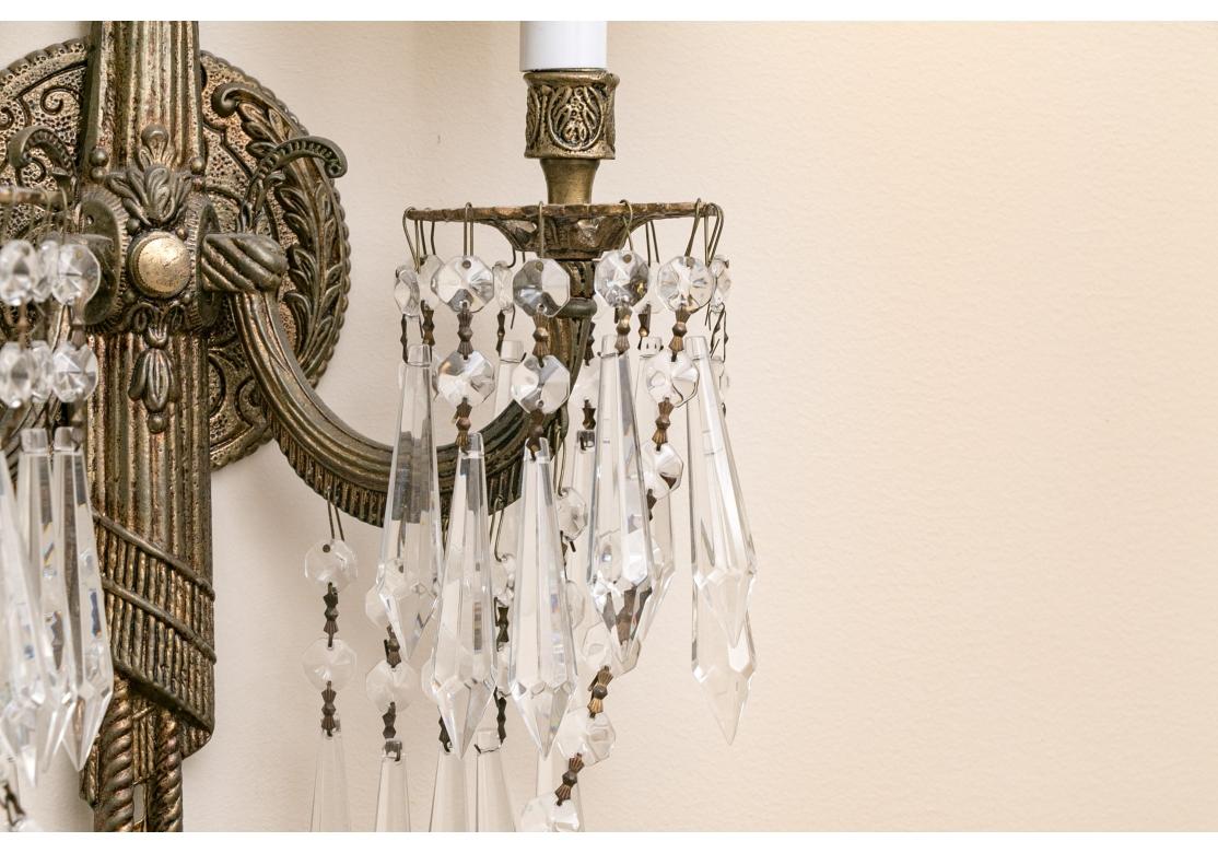 A fine pair of French style two light wall sconces more than likely produced in Spain in the 1960's. The sconces present with fine quality faceted crystal pendants around each bobeche and along the arms, draped bead chains and come with silk pleated