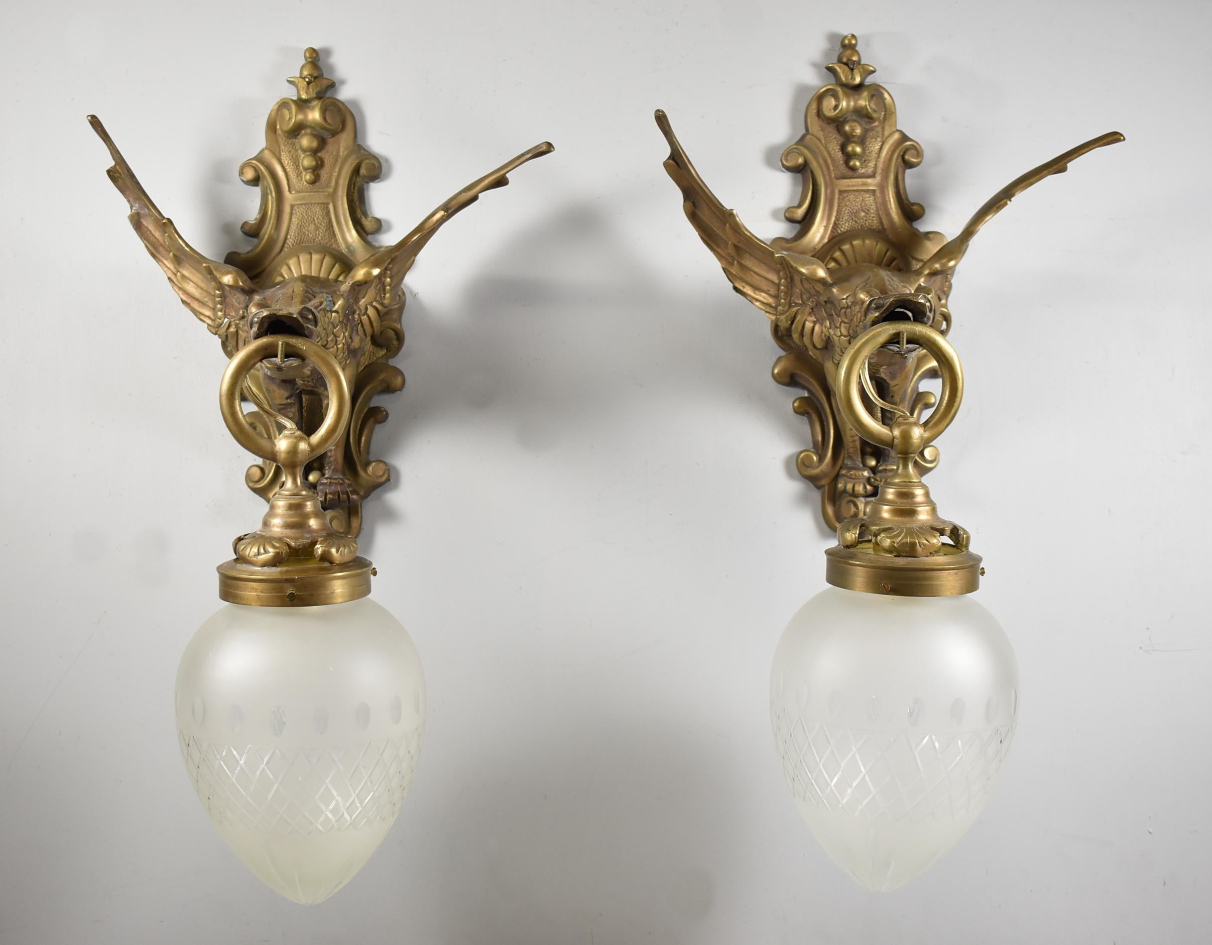 Pair of gargoyle bronze Gothic style wall sconces. Ring in mouth holds fitter single socket with bullet shaped cut and polished satin glass shades.
