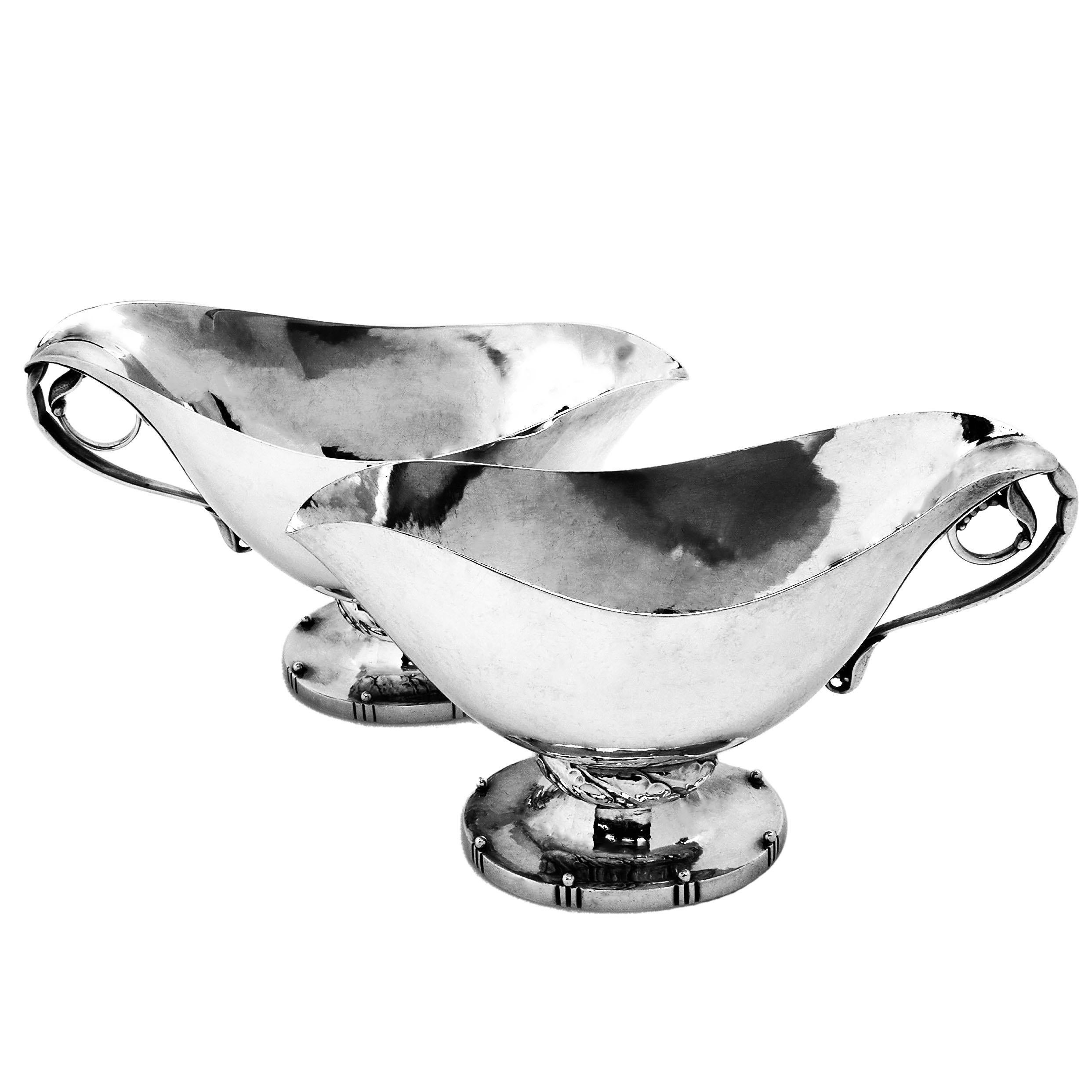 A pair of magnificent Sterling Silver Sauce Boats by Georg Jensen with gorgeous blossom inspired handles. Each Gravy Boat stands on an oval spread foot and the body of each sauce boat is very lightly hammered. There is a chased patterned band