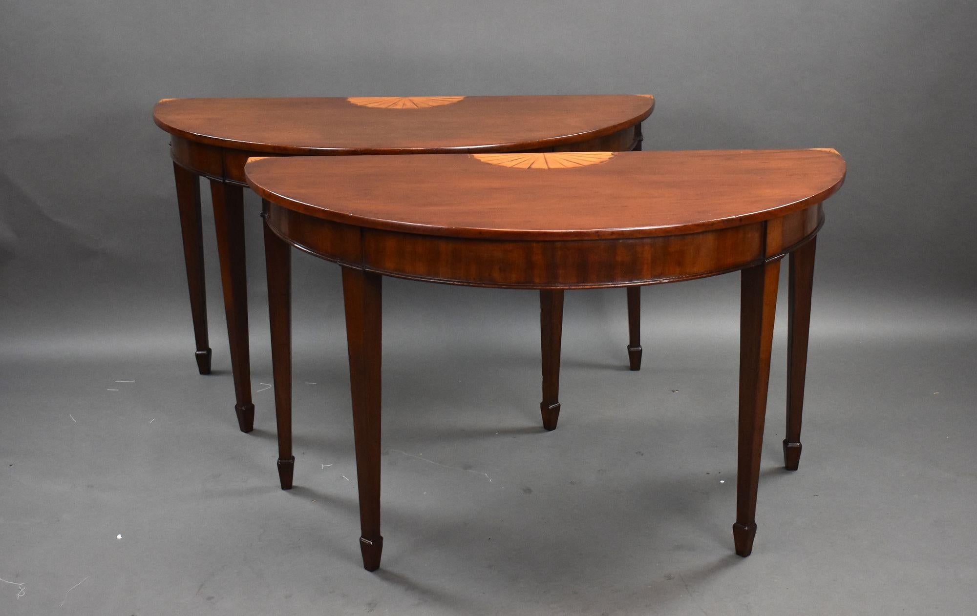 A fine pair of Georgian inlaid mahogany console tables of exceptional craftsmanship. Each table features a beautifully figured mahogany top with intricate fan inlays to the center and corners. The elegant demi-lune shape is supported by slender,