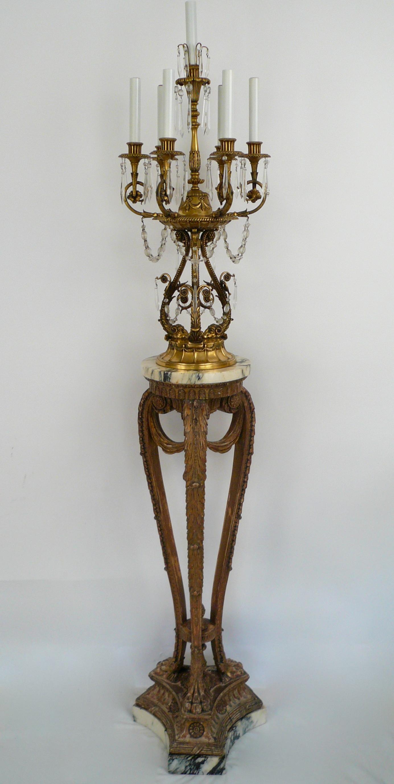 These amazing gilt bronze girandole form candelabra feature Robert Adam style decoration, including swag, rams heads, and acanthus leaves. They retain the original marble and carved giltwood stands, and are pictured in the E. F. Caldwell