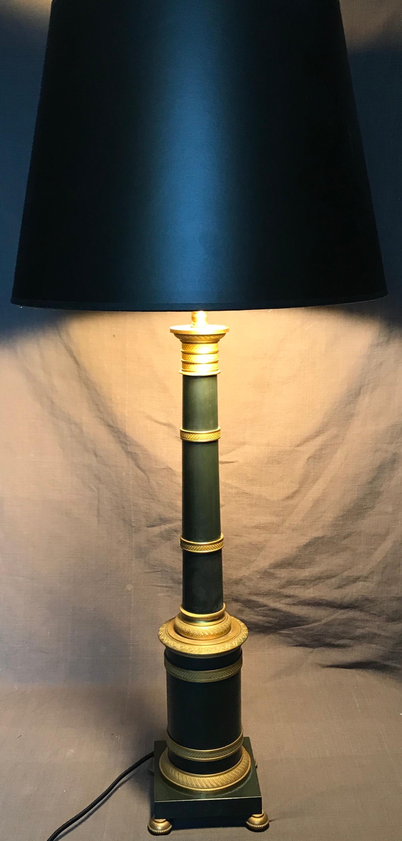 Pair of gilt and patinated metal banded column lamps. Empire style modern lamps with crisp gilt banding on dull green patinated shafts; newly rewired with black silk cording. Slight mottling to green patina on one lamp. France, 20th