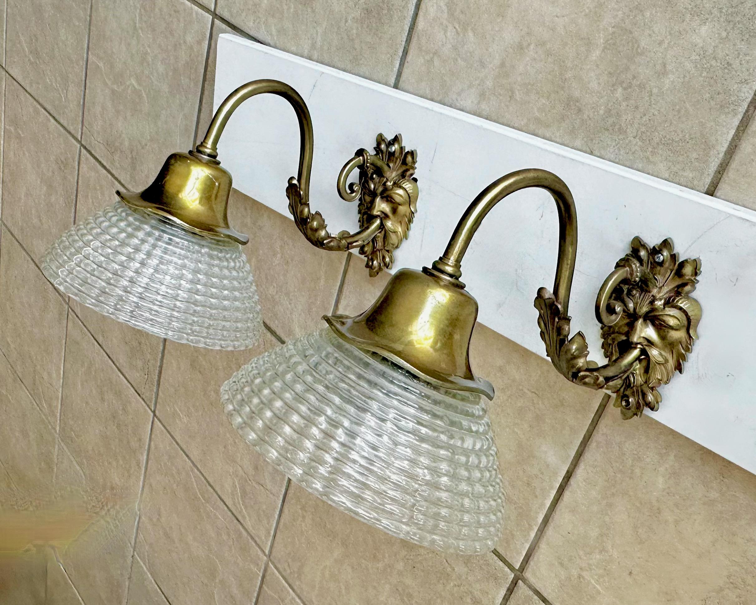 Paire d'appliques murales en laiton français doré à motif de tête de satyre mythologique, avec des abat-jours en verre texturé. Nouveau câblage pour l'installation aux États-Unis. Chaque lampe fonctionne avec une seule ampoule à culot A. Diamètre du