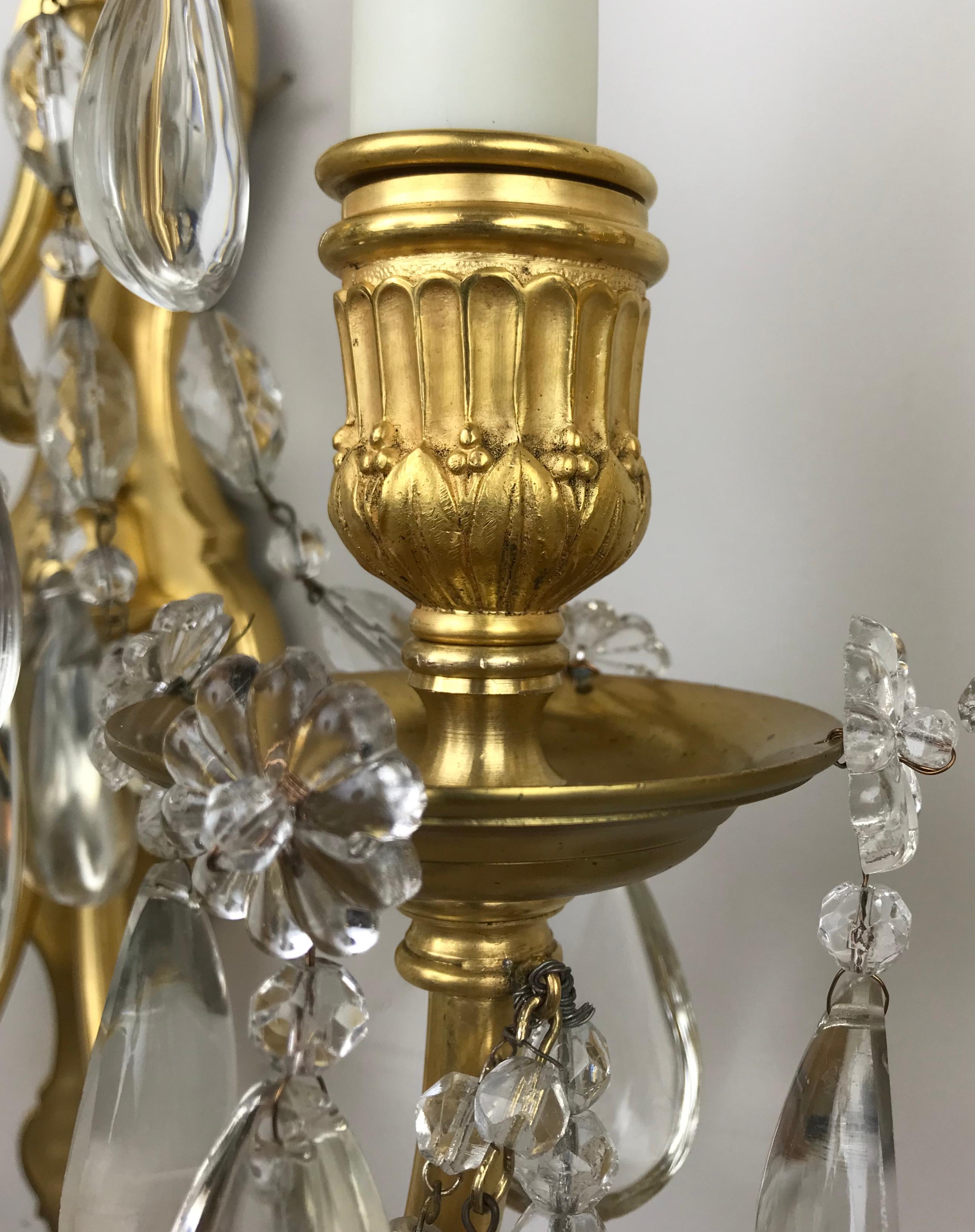 This impressive pair of Louis XVI style bronze sconces by the famed maker Edward F. C Caldwell feature cast and hand chased gilt bronze candle cups with Classical motifs, cabochon form crystal drops, and cut crystal obelisk form finials. They are