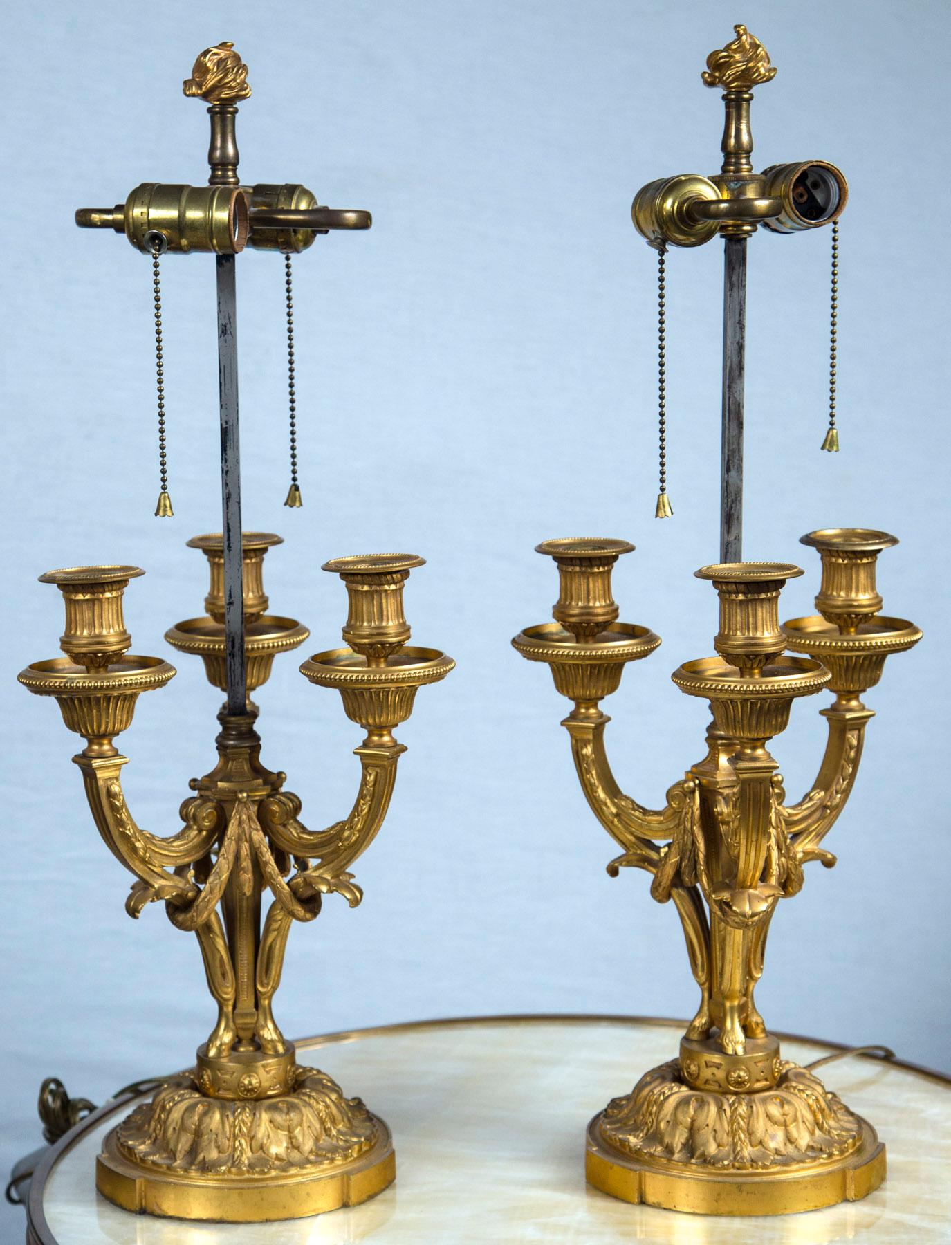 In the Louis XVI neoclassical style. Each with 3 candle arms. Decorated with acanthus leaves and swags. Very well chased and of great quality.
Square steel rod supports light cluster. Gilt bronze flame finial.