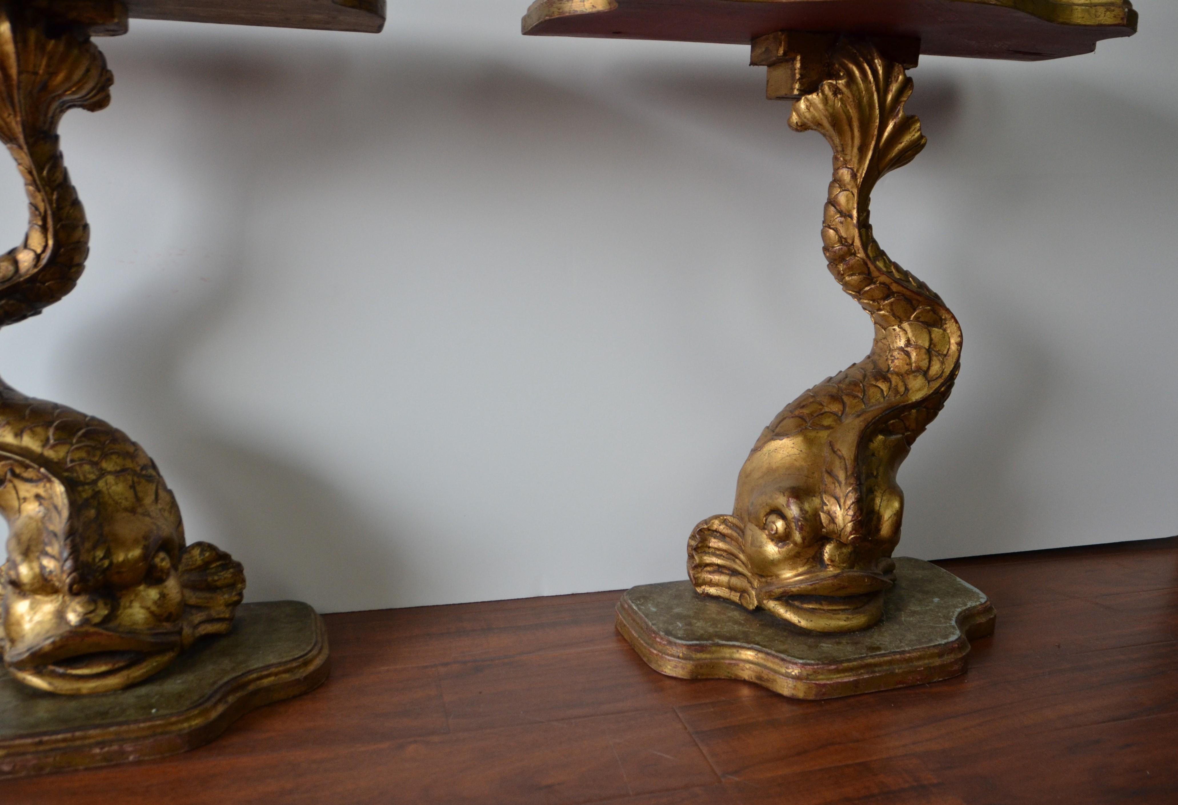 A very decorative pair of gilt finished end tables with the supports designed as dolphin style sea-creatures. The tables are serpentine fronted, hand carved wood and fitted with glass tops.
