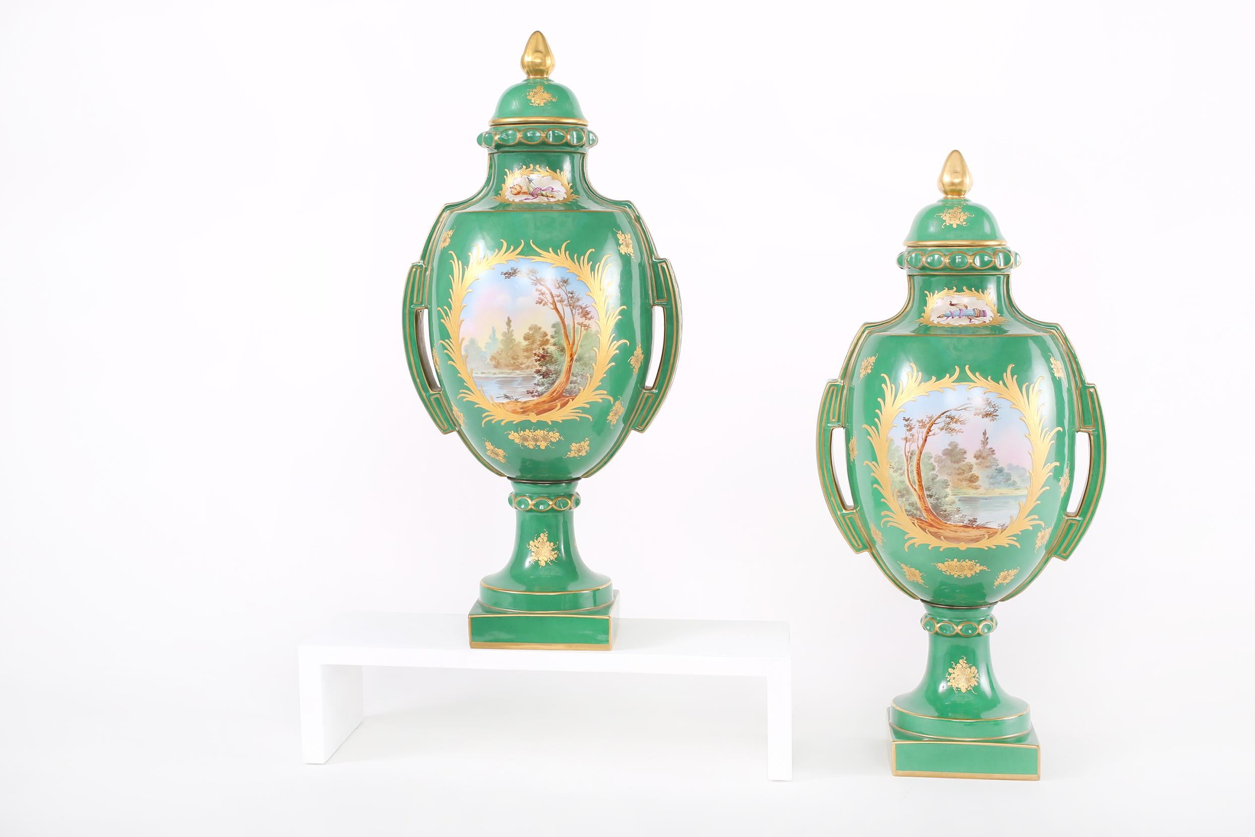 Pair gilt porcelain Dresden covered decorative urns / pieces with exterior painted scene design details. Each urn is in great condition with appropriate wear consistent with age / use. Maker's mark undersigned. Each piece stands about 20.5 inches
