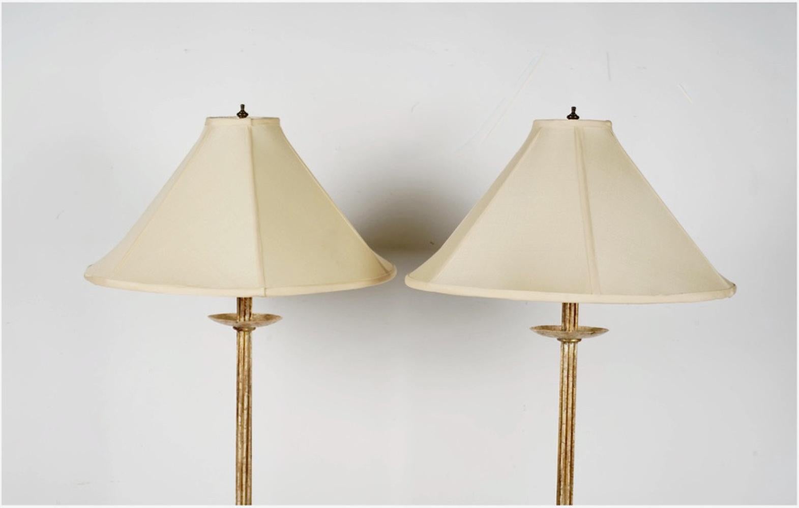This is a handsome pair of late 20th century wrought iron floor lamps that have been gold leafed. The lamps feature a three-legged arching base supporting a multiple rod column terminating in an iron candle cup with electrical fittings. The lamps