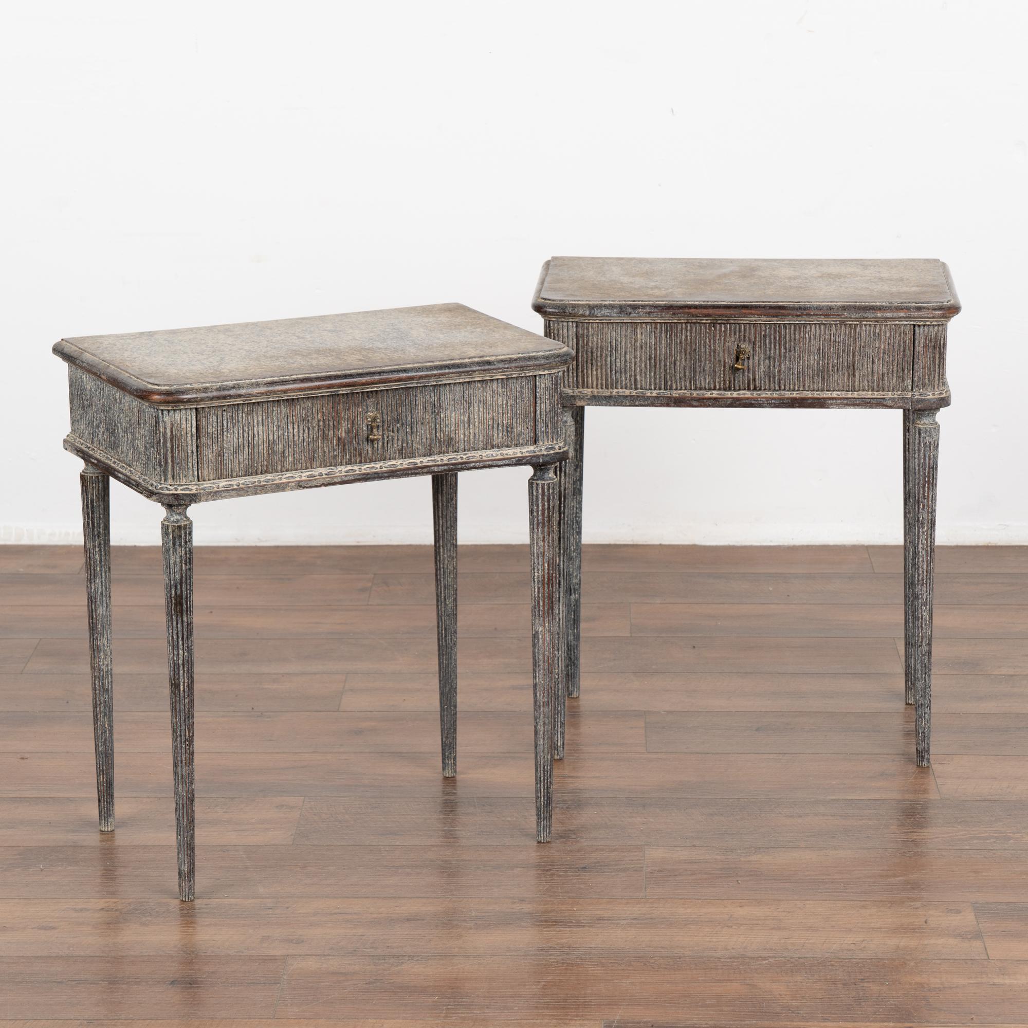 Pair, Swedish Gustavian style side tables with fluted skirt and single drawer resting on graceful fluted turned legs.
Restored, later professionally painted in layered/mottled shades of gray with plum undertones and white overtones all lightly
