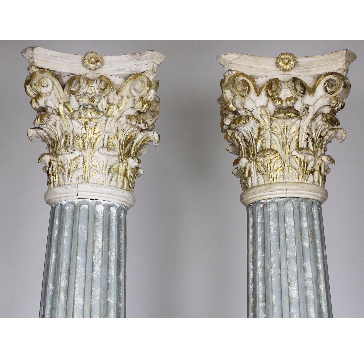 A large pair of Greco-Roman style carved wood and gesso carved faux-marble and parcel-gilt architectural Corinthian columns. The slender carved walnut column resting on a square plinth and crowned with a white and parcel-gilt carved cast gesso