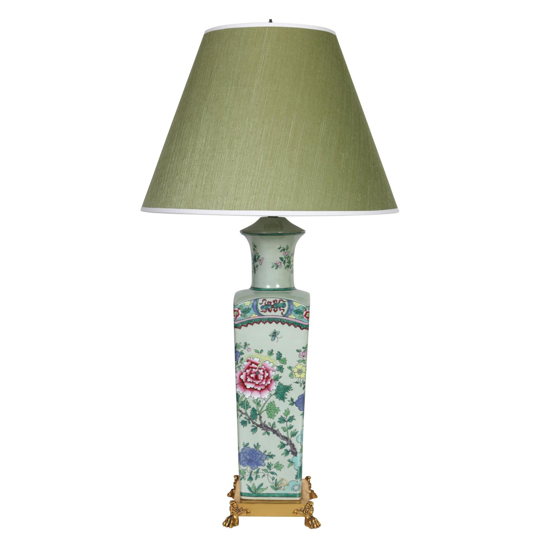 A pair of green chinoiserie porcelain lamps with brass feet. The tall vintage lamps are decorated in a beautiful Asian style with detailed and vivid pink-red and blue flowers, vines and birds with large colorful tail feathers. The lamps sit on a