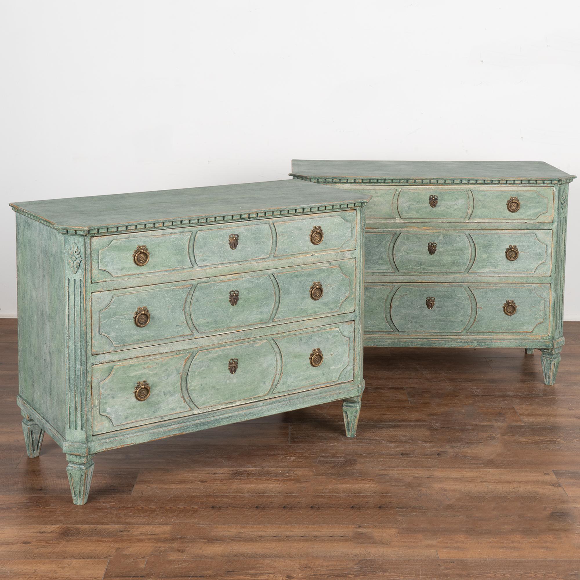 A pair of elegant Gustavian pine chests of three drawers painted in soft shades of green.
Canted fluted side posts with upper carved floral medallion, dentil molding, raised on four tapered fluted feet.
The decorative raised panels on each drawer