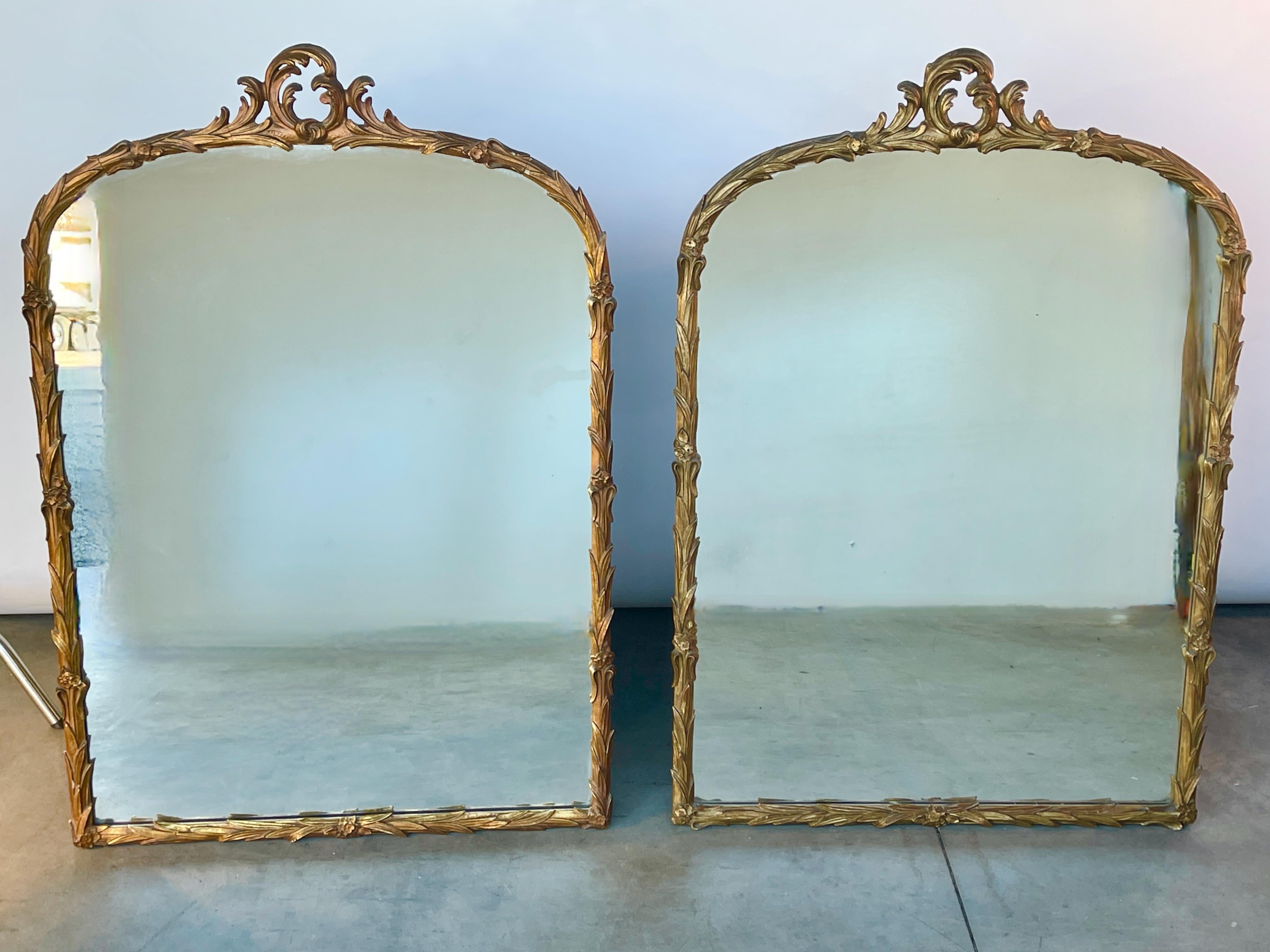 Pair of art deco wall mirrors by Grosfeld House circa 1939. 
Hand carved wood in a palm leaf design applied with gold leaf and gesso. 
Measures: 6 inches high to scrolled top by 32 inches wide.
