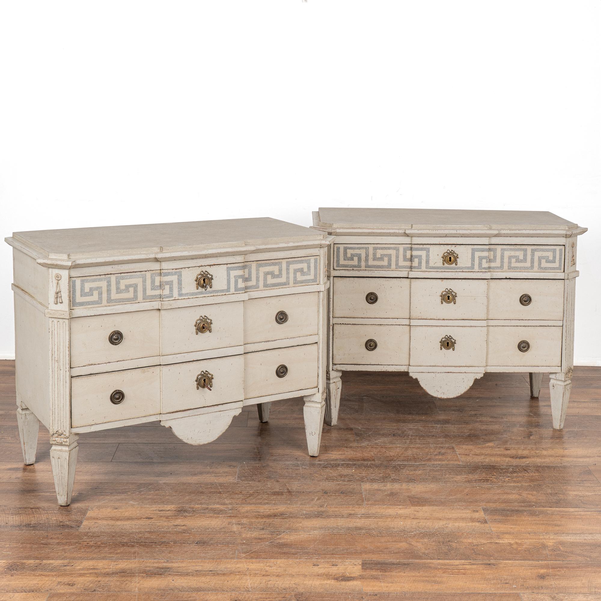 A pair of decorative Gustavian pine chest of drawers with Greek key motif painted along upper drawer.
Canted fluted side posts topped with carved applied tassels resting on four tapered feet.
The newer, professionally applied antique white custom
