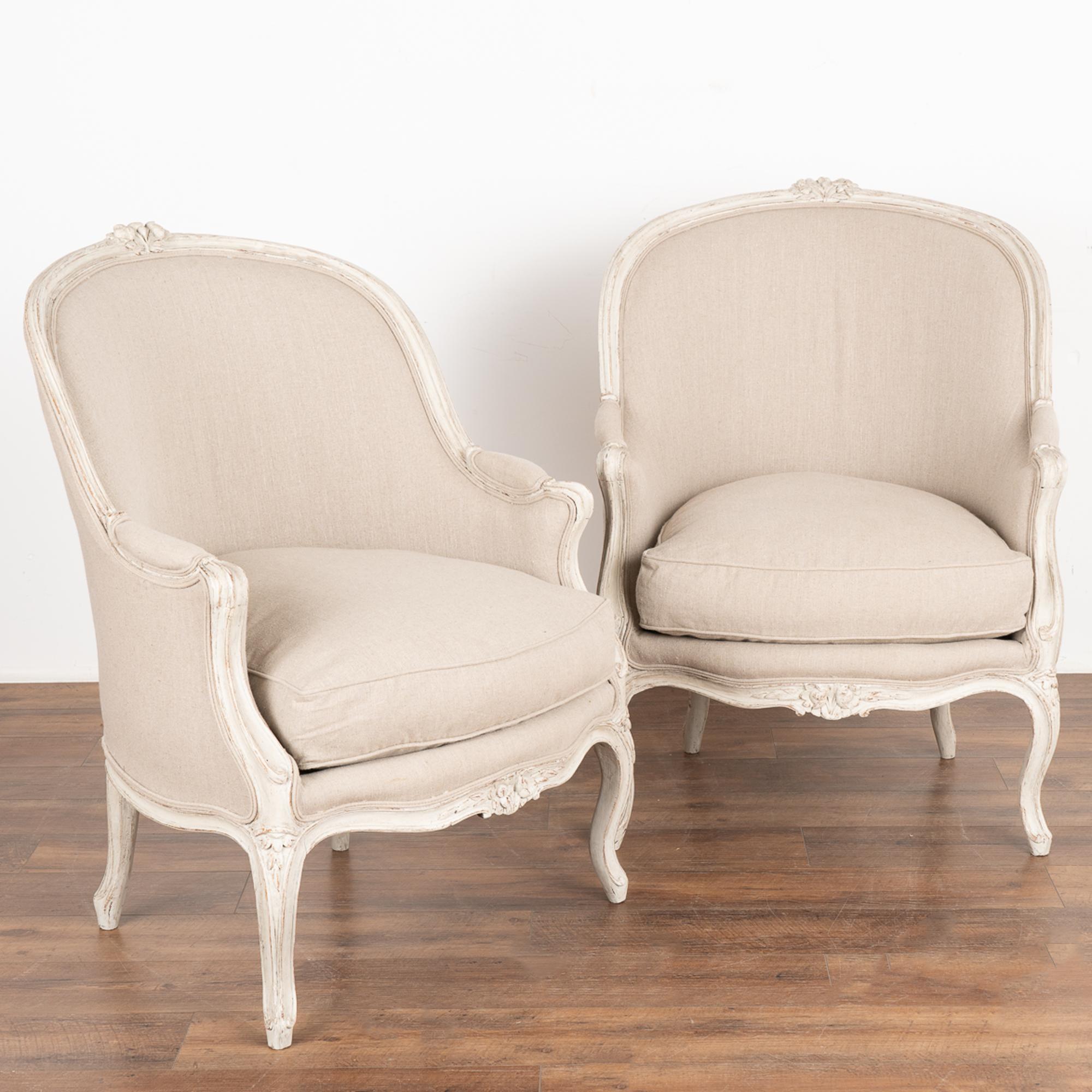 Pair, attractive Swedish country Gustavian arm chairs with gently curved barrel back and carved flowers adorning the  back and skirt.
Newer, professionally applied layered white painted finish has been lightly distressed, adding to the grace of
