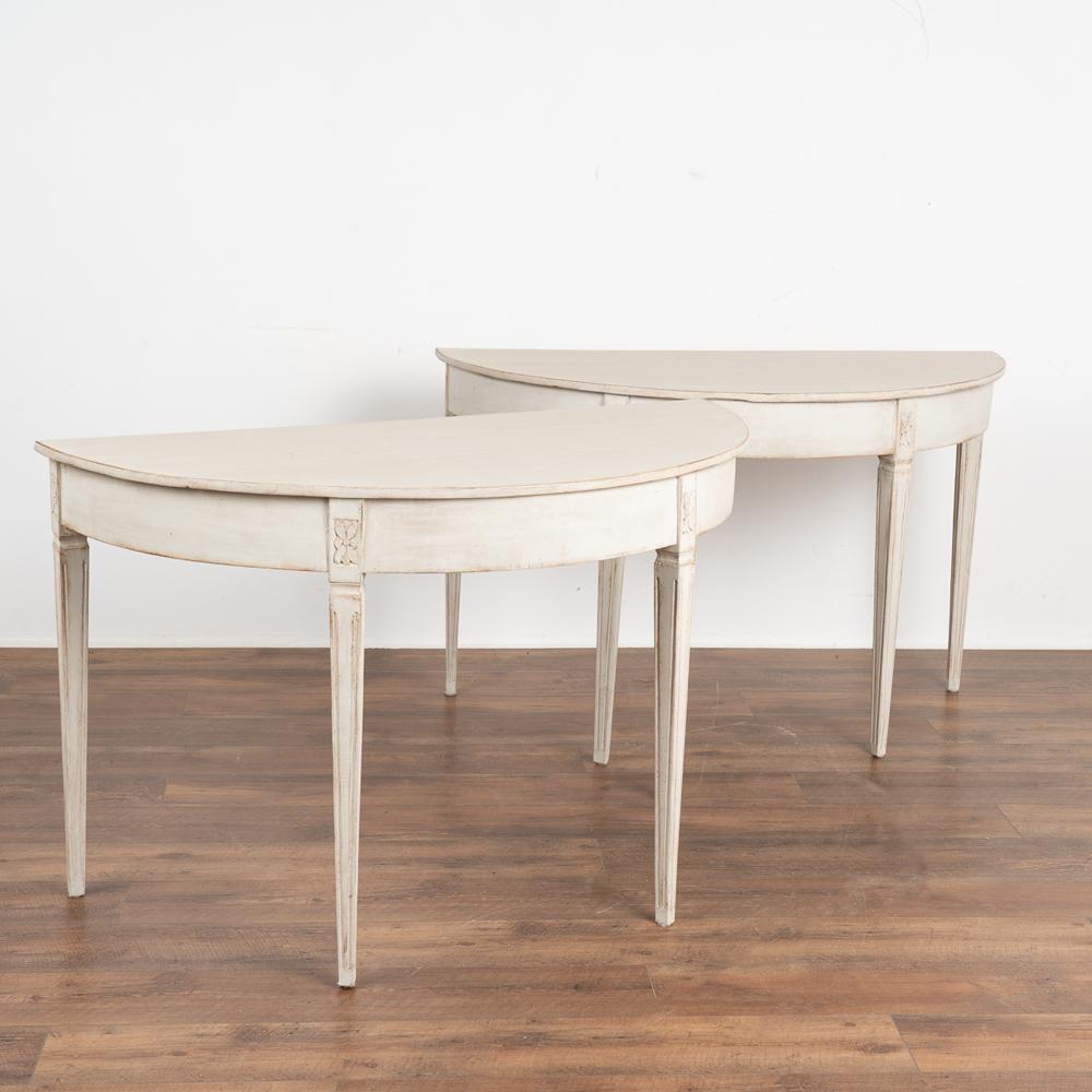 Pair, Gustavian demi-lune side tables or consoles. 
Gently tapered fluted legs topped with simple decorative floral carving.
Newer professionally applied layered white painted finish (with soft gray undertones), slightly distressed to fit the age