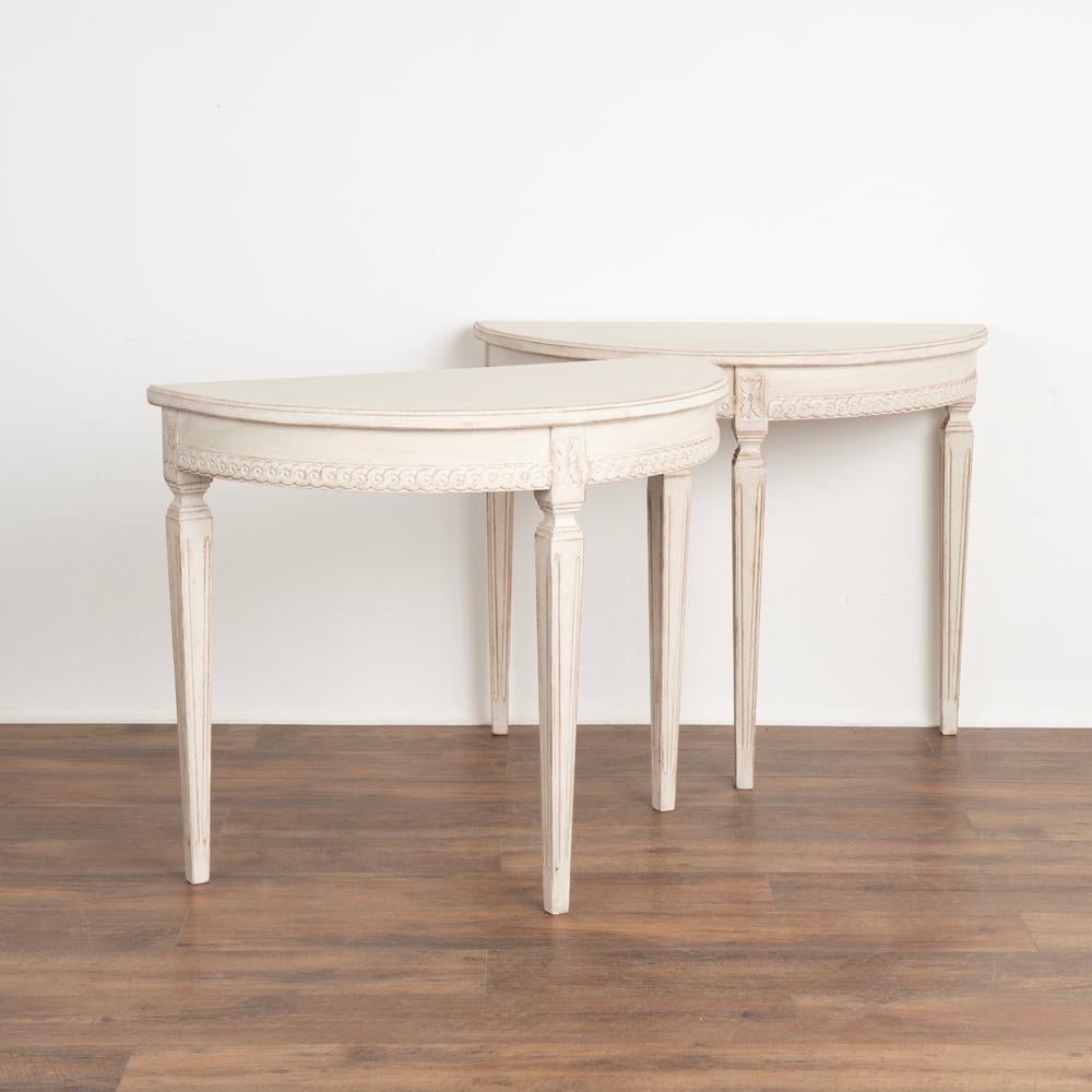 Pair, gustavian demi-lune side tables or consoles. 
Gently tapered fluted legs and decorative carving along skirt.
Newer professionally applied layered white painted finish, slightly distressed to fit age and grace of the tables.
Restored, strong