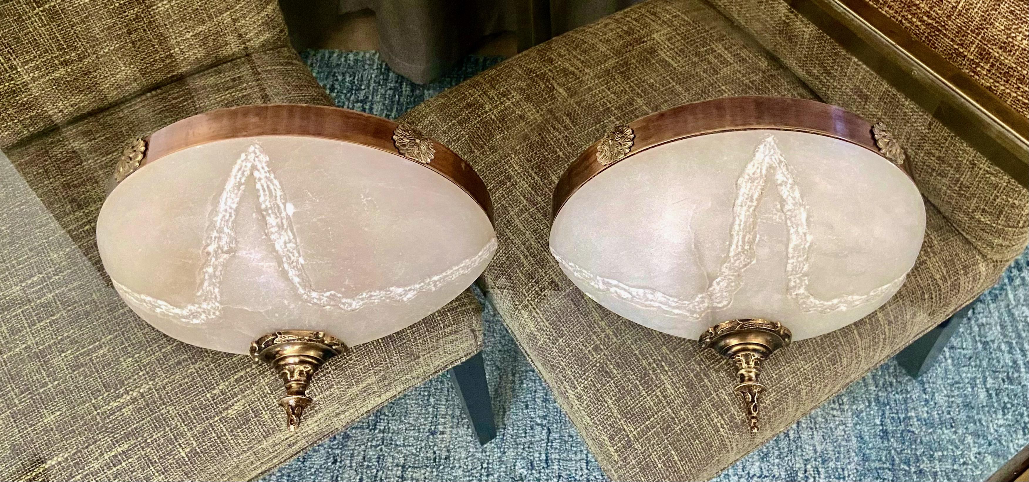 Pair of French Louis XVI style alabaster half moon or quarter shape wall sconces. The alabaster has an etched stylized design pattern providing unique effect when lit. The sconces are enhanced with decorative brass antiqued fittings. Each uses