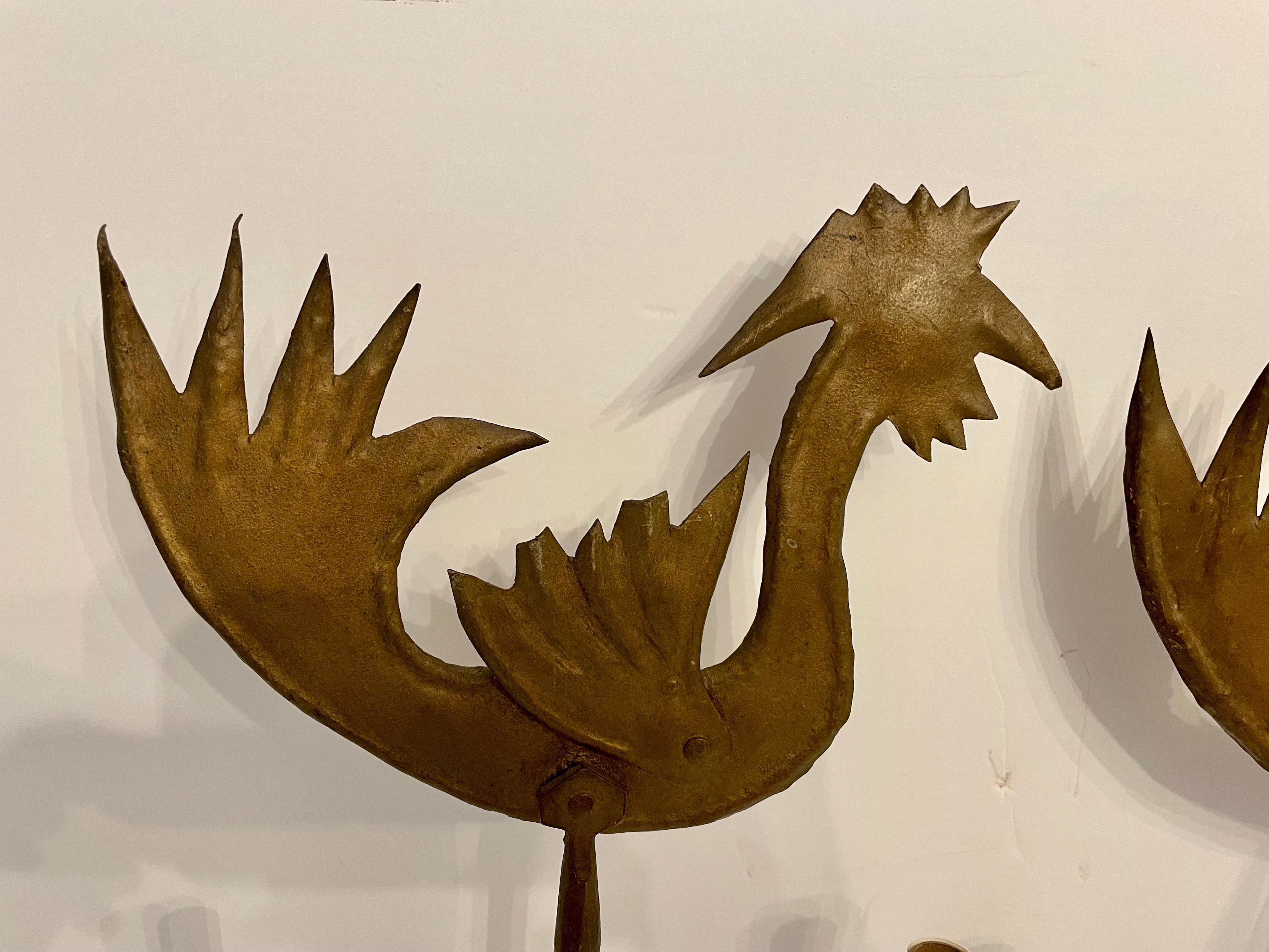 Pair handmade gilt iron rooster sconces. Two Arms each. Hand wrought iron with cut metal rooster, all with gilt finish. Some patina to finish. Wired, ready to use. Hook on back for hanging. Measures 26
