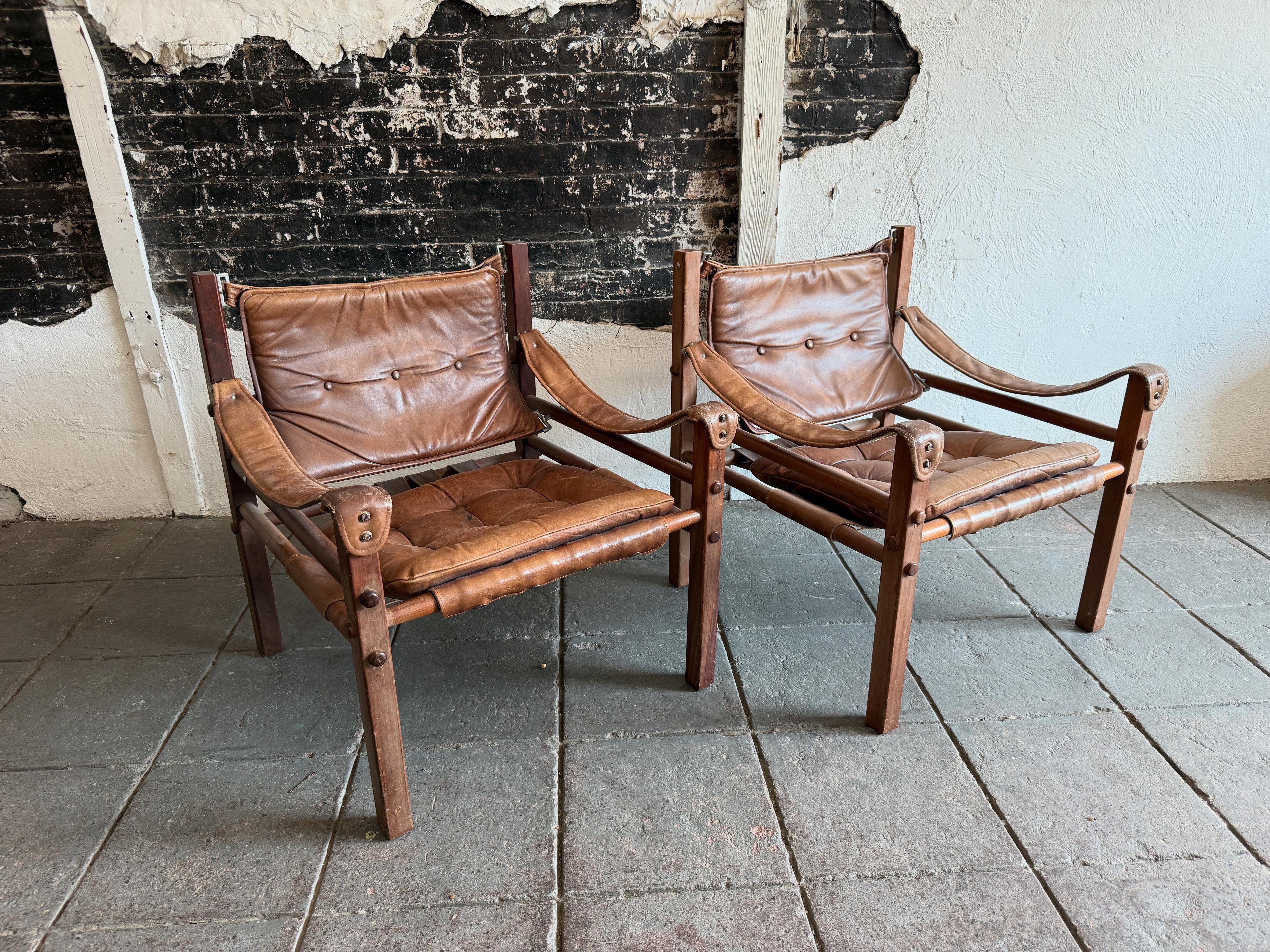 Pareja de bonitos sillones safari modernos de mediados de siglo al estilo de Arne Norell. Precioso asiento de cuero marrón desgastado envejecido con pátina y toneladas de carácter. Tiene un robusto armazón cuadrado de madera dura con asientos de