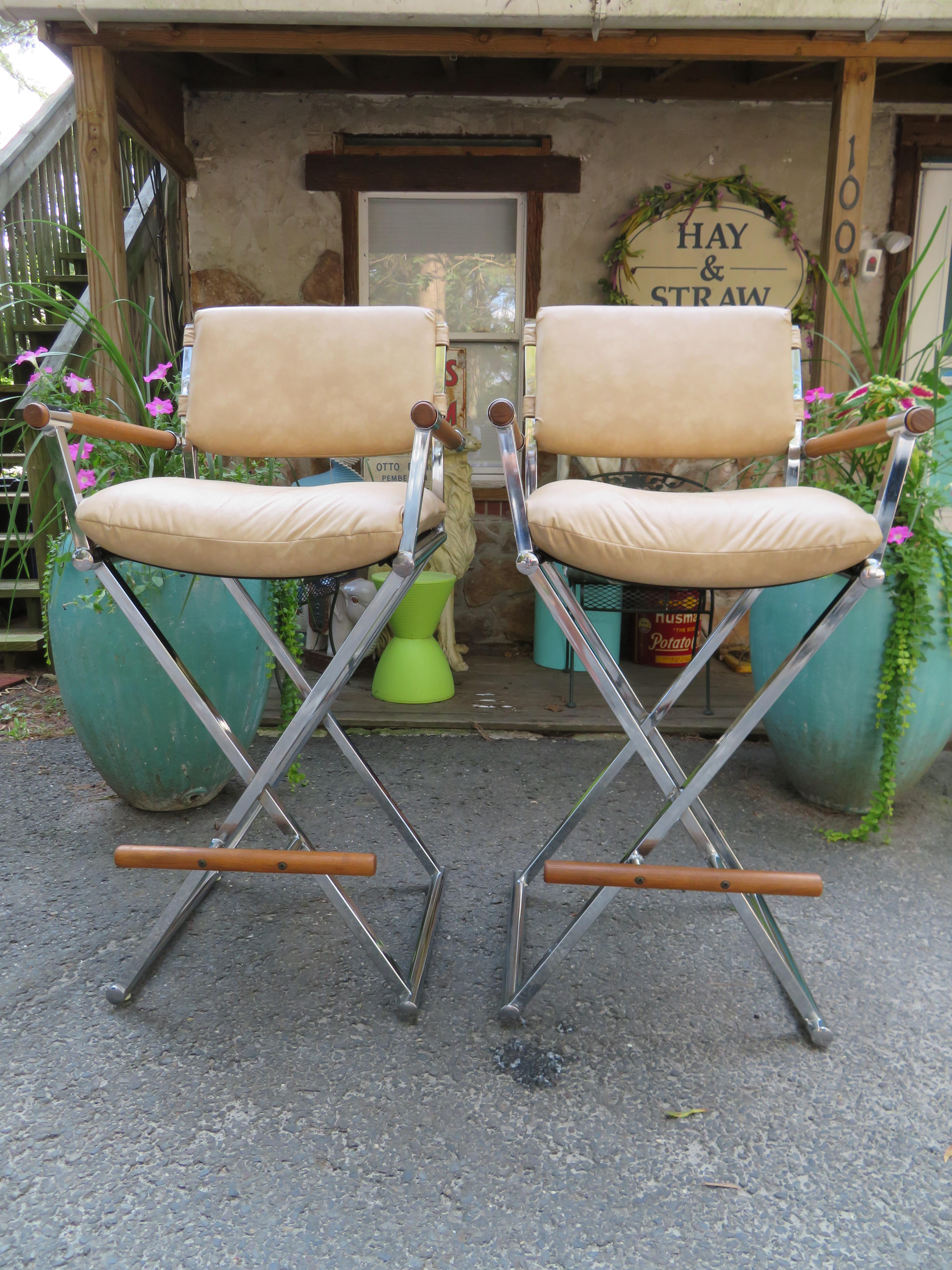 A vintage pair of director's chair bar stools in tan faux leather with chrome X-base frames and wooden arm rests attributed to Milo Baughman. The seat height on these is 32 T and they measure 45