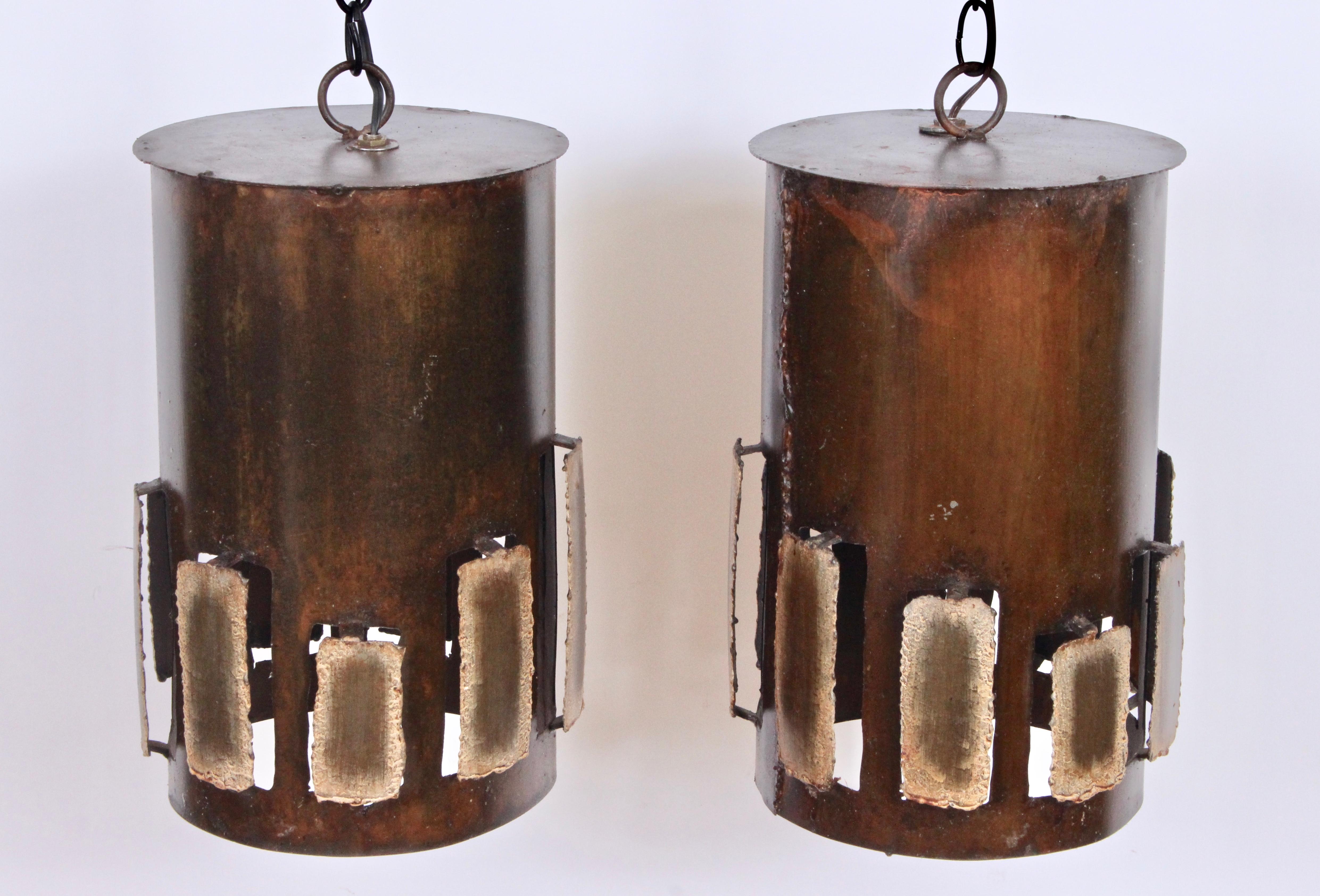 Pair of large art studio torched Brutalist brass hanging lamps in the manner of Harry Balmer, 1960s. Featuring handcrafted vented brass cylinders with applied cut outs and patinated bronze brass appearance. With brass loop ring top. With 2 5.5