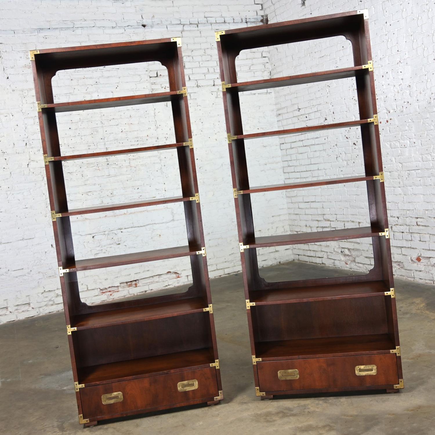 Handsome vintage Campaign style walnut bookcases, display units, or shelves with antiqued brass details by Henredon, a pair. Beautiful condition, keeping in mind that these are vintage and not new so will have signs of use and wear even if it has